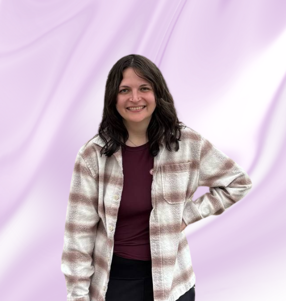 A woman stands smiling with her right hand on her hip against a pink and purple abstract background, wearing a plaid jacket and a maroon shirt.