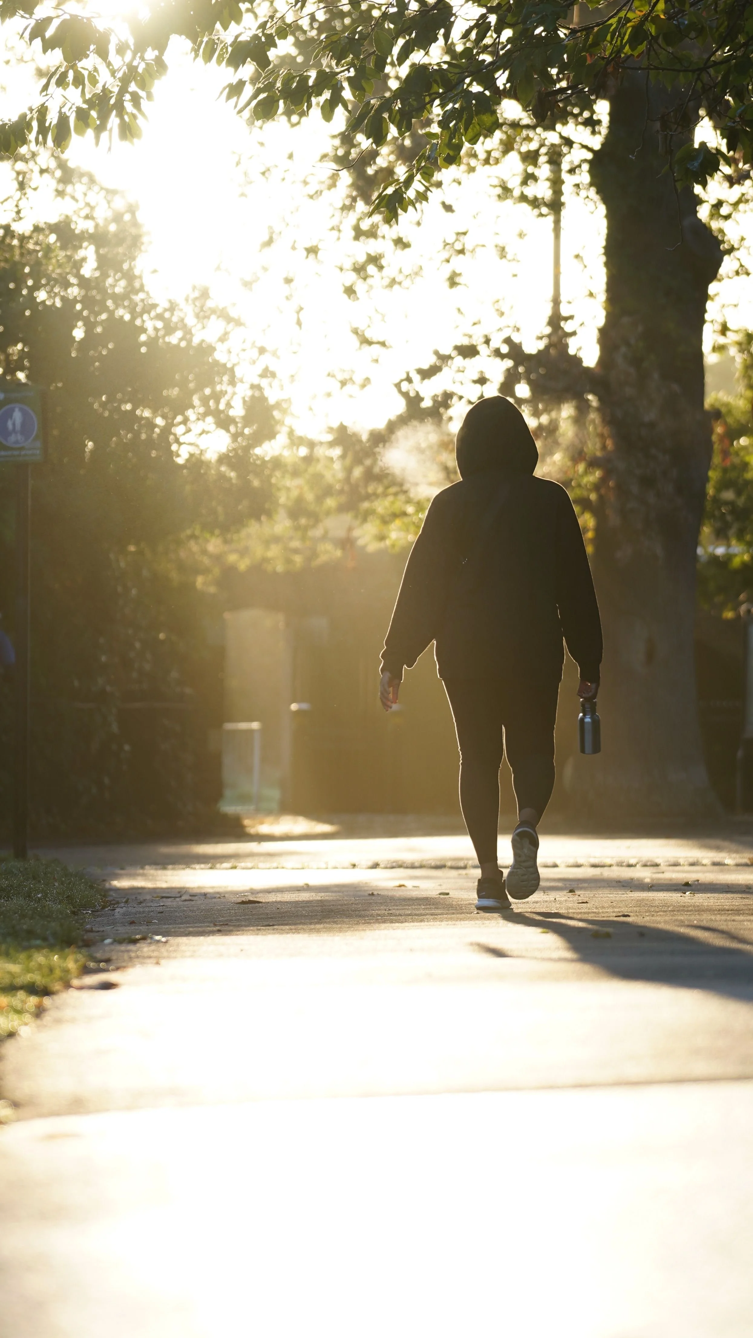 Person walking by themselves on the street holding a waterbottle