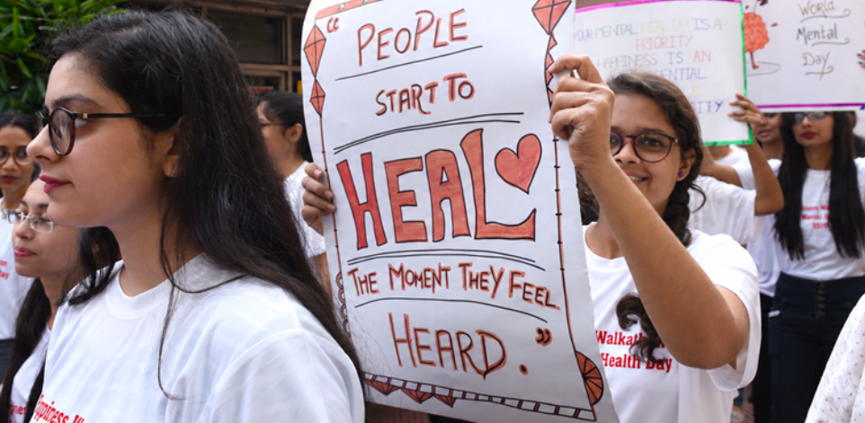 A young girl hold a white sign that says "people start to heal the moment they feel heard."