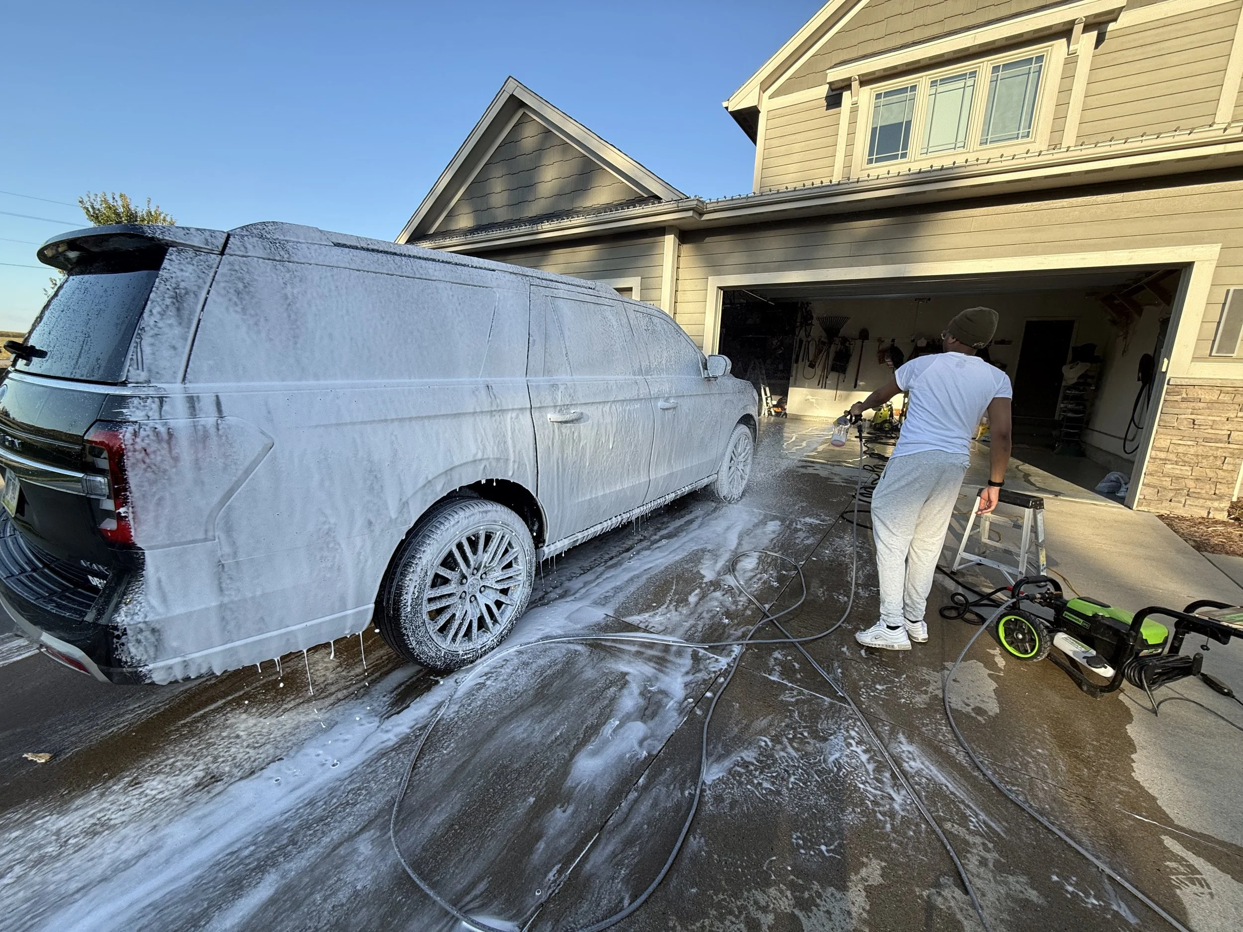 A person washing a black SUV with soap in the driveway of a house