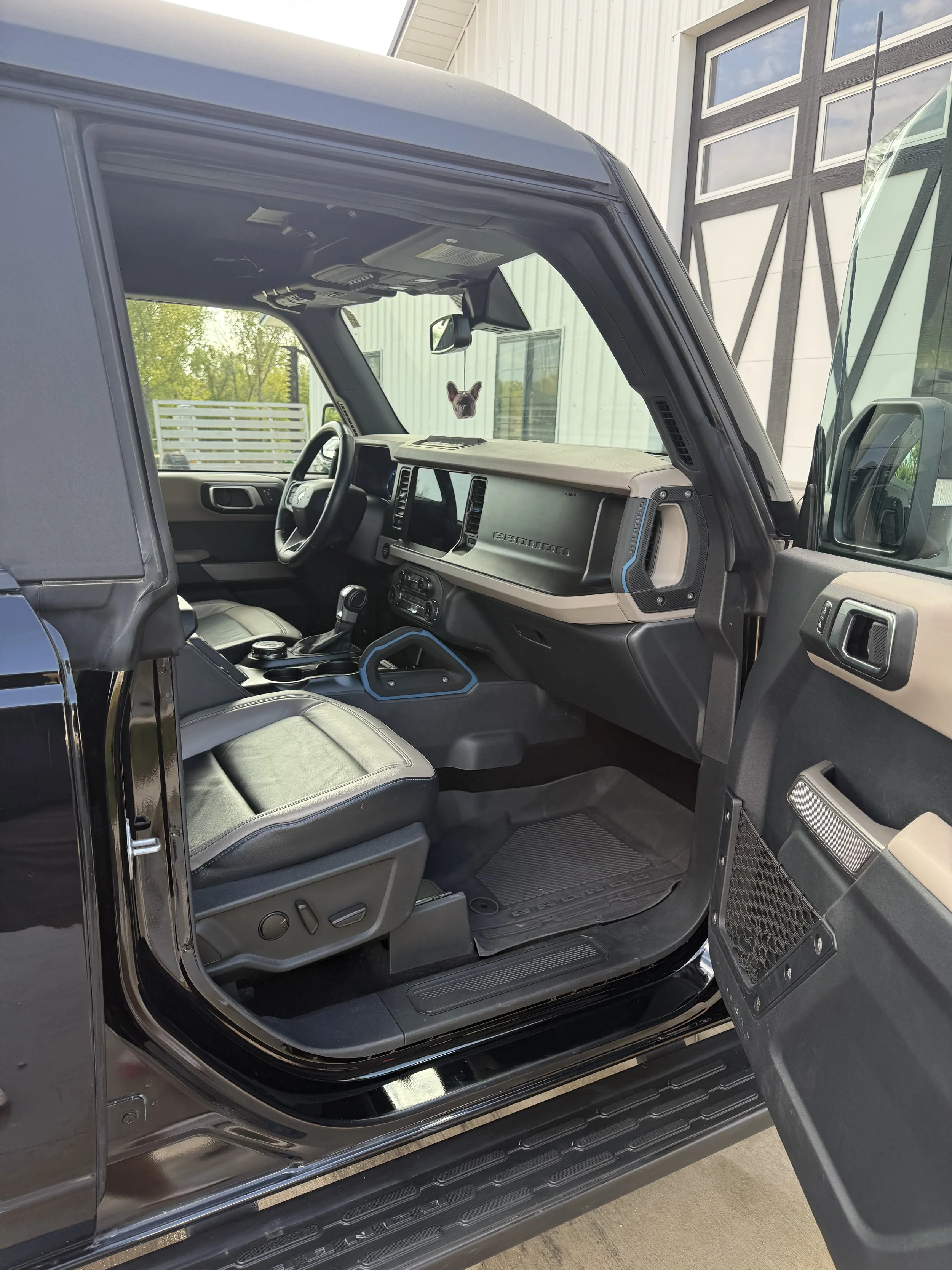 Interior view of a black off-road vehicle showing the driver's seat, dashboard, and steering wheel, with a small dog sticker on the windshield.