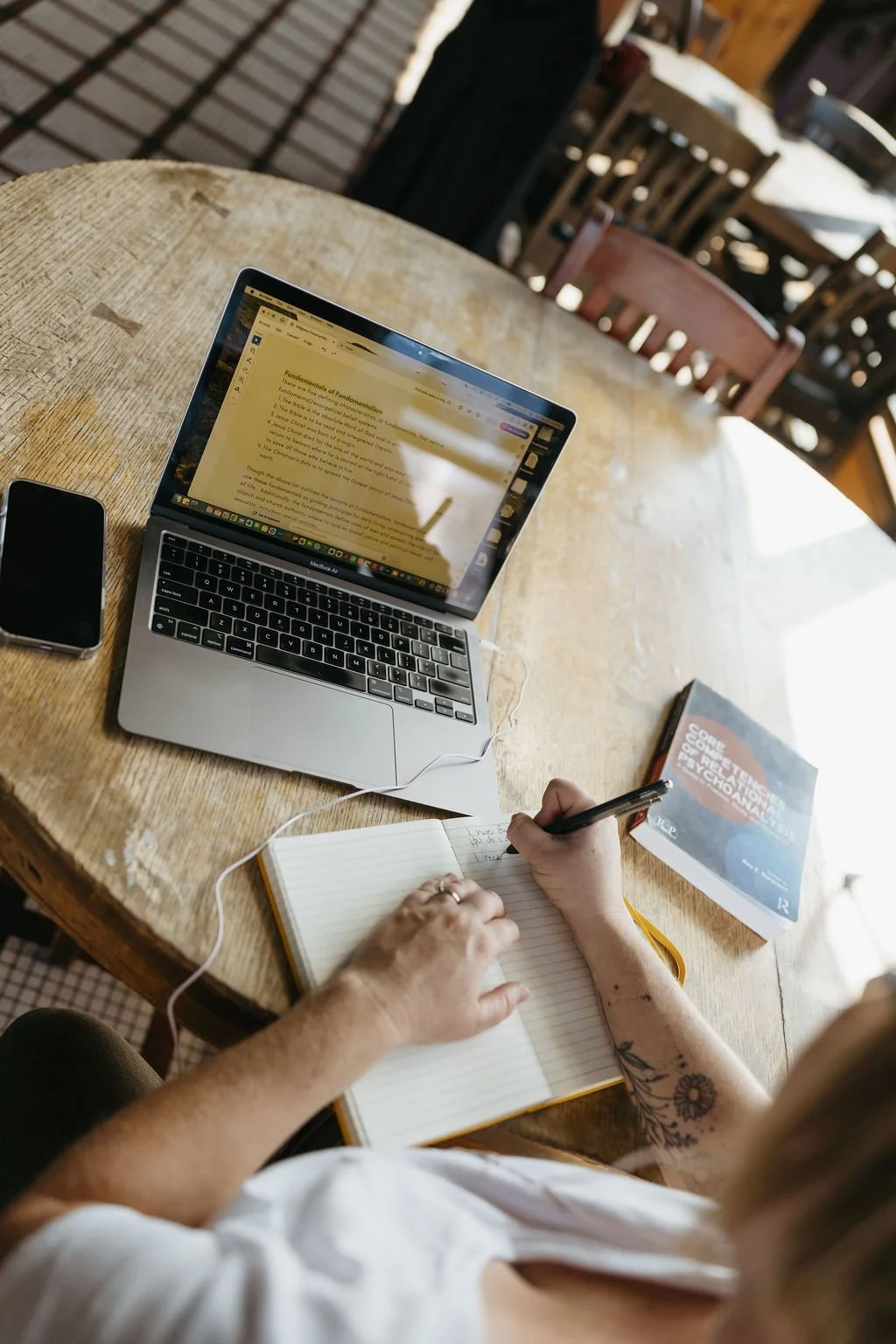 Laptop open while woman writes in a journal