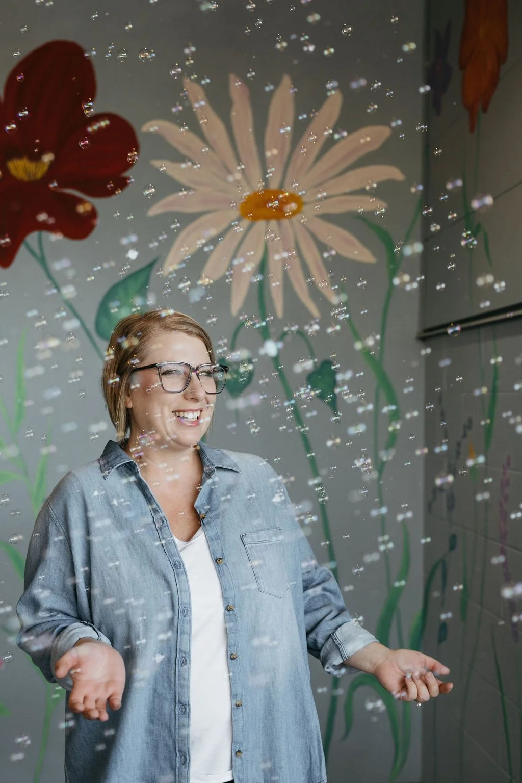 A woman with bubbles floating around her and a flower mural behind her.