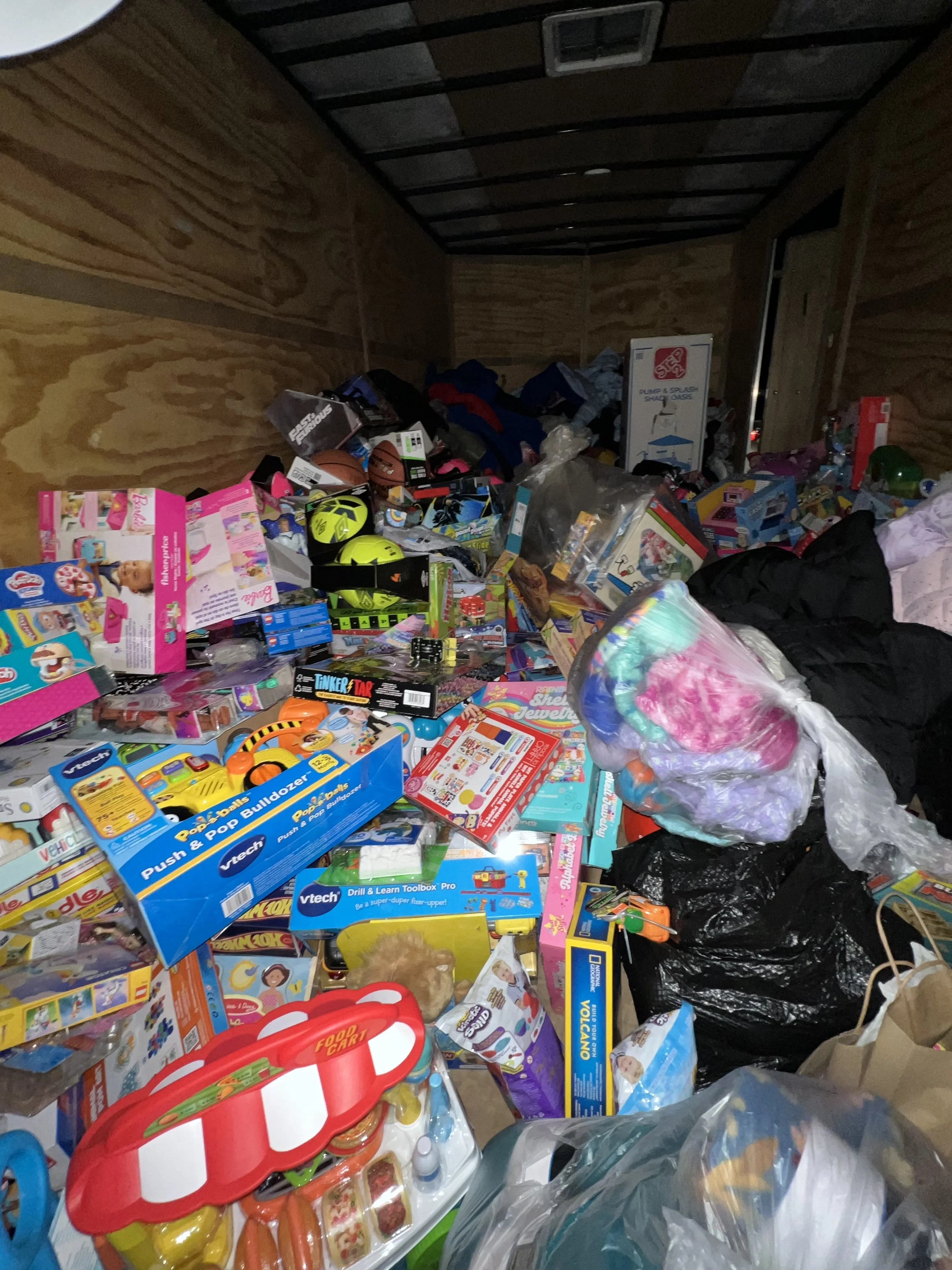 A storage unit filled with various toys, including stuffed animals, plastic building sets, balls, and packaged children's toys, along with miscellaneous items like plastic bags and clothing.