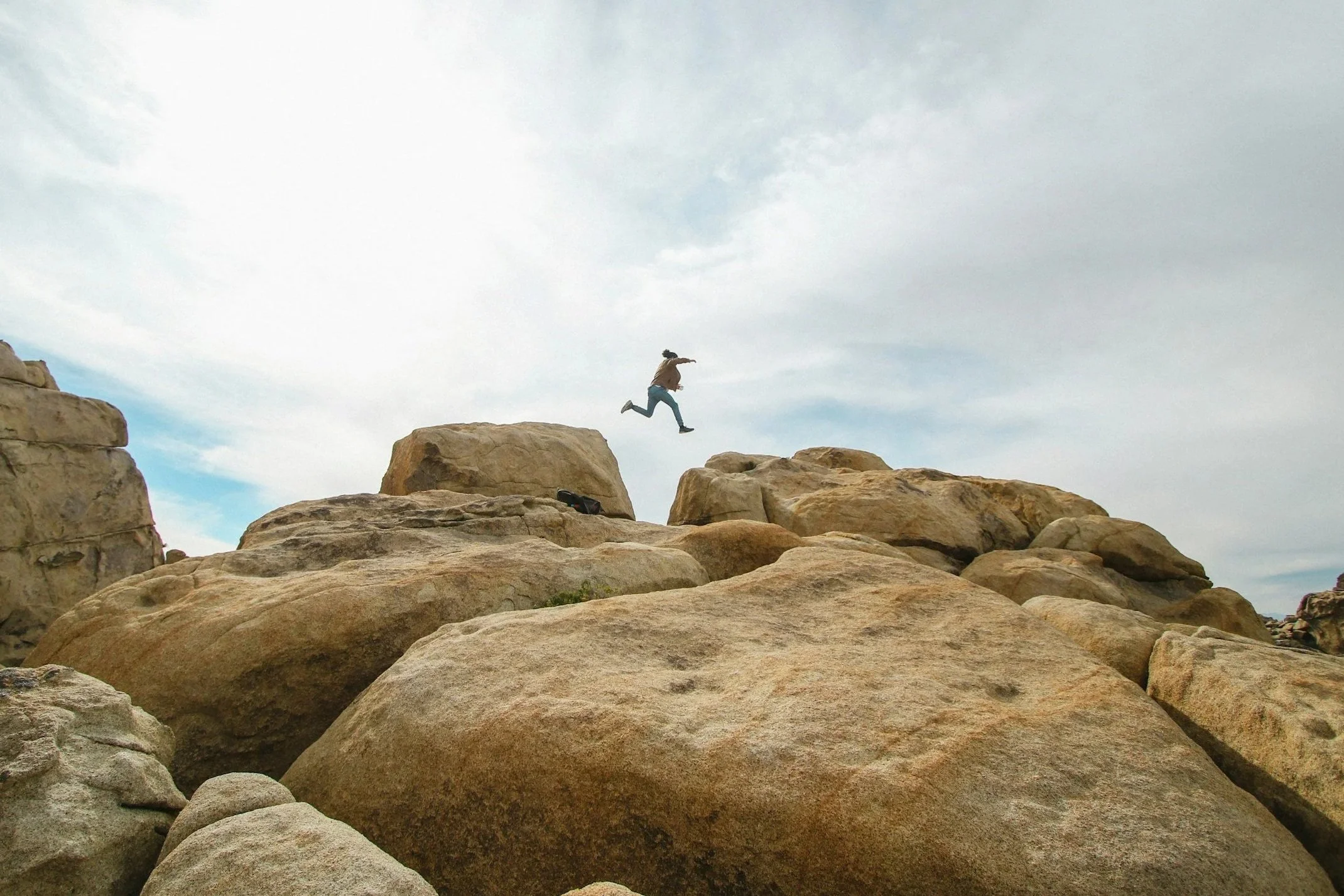 A person jumping between large boulders on a rocky landscape under a cloudy sky.