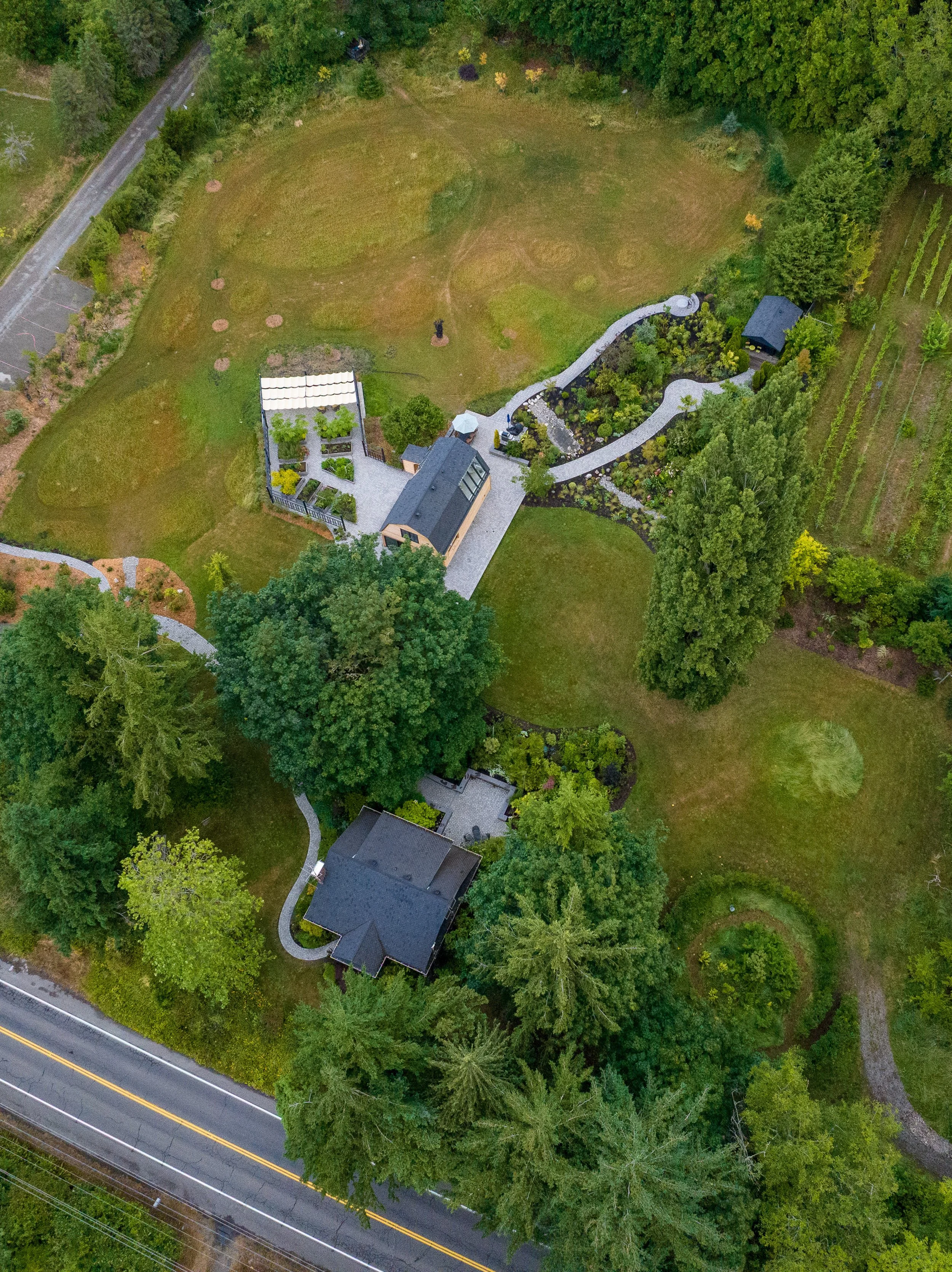 Aerial view of a large property with two houses, surrounded by trees, lawns, a garden, a winding pathway, and a road at the bottom.
