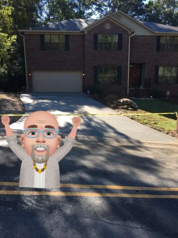 A house with a driveway, two trees in the background, and a cartoon avatar of a man with glasses, a beard, wearing a grey shirt and yellow necklace, holding a yellow tape stretched across the road in front of the house.