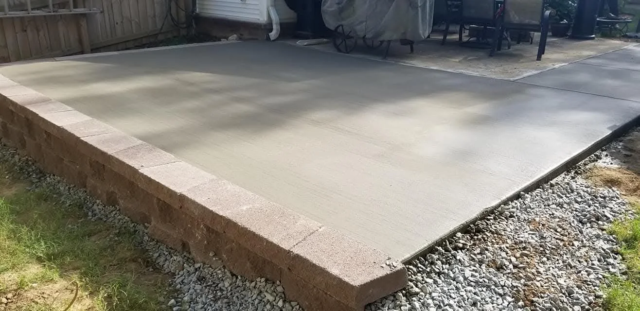 Freshly poured concrete slab in a backyard with outdoor furniture and a wooden fence.