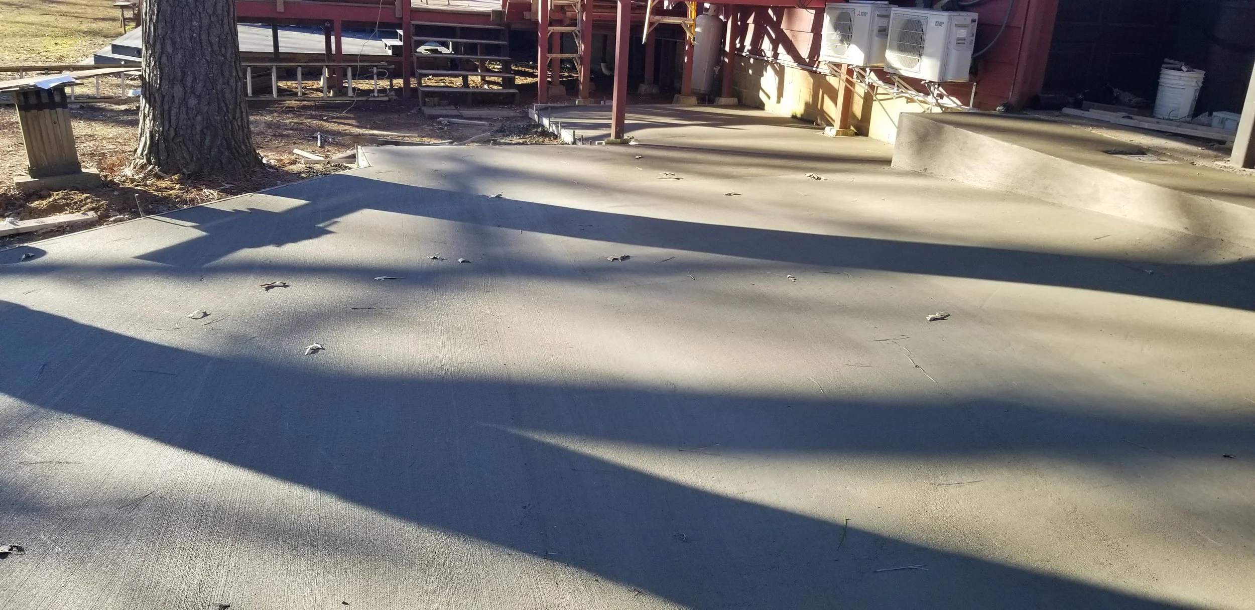 Construction site with freshly poured concrete sidewalk, a tree on the left, and building scaffolding in the background.