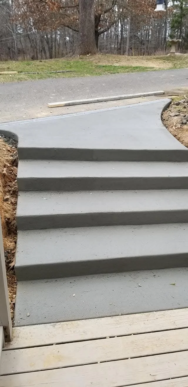 Custom concrete steps connecting a driveway to the deck to the which is ground level to the home.