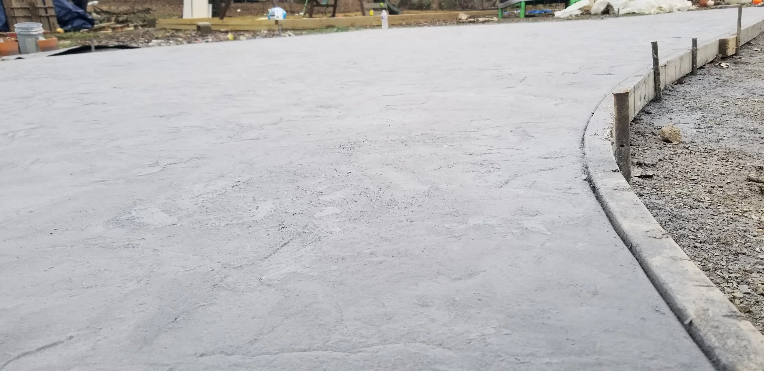 Freshly poured concrete sidewalk with wooden form boards along the edge, in a residential construction site.