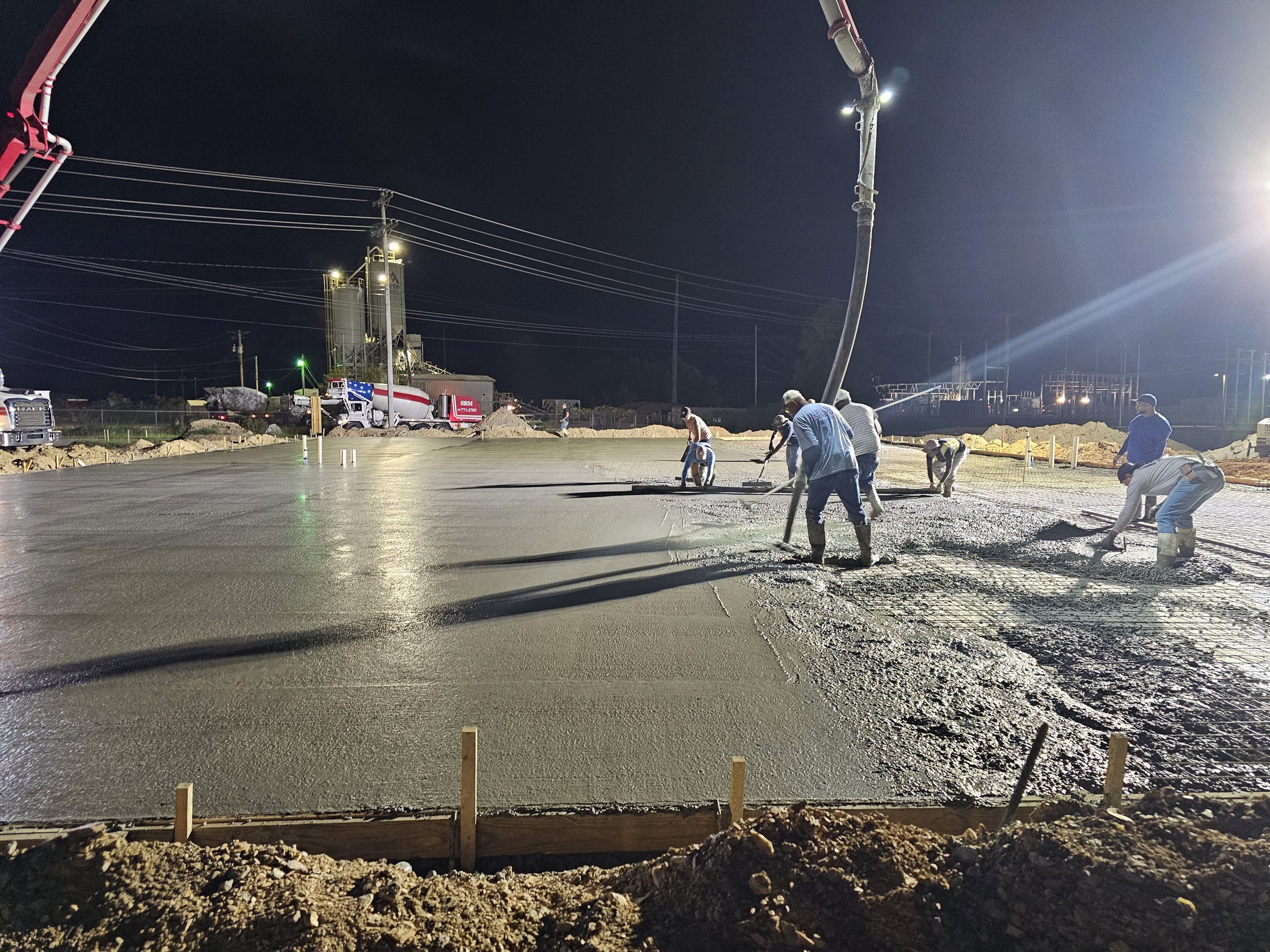 Workers pouring and leveling wet concrete at a construction site during night time.
