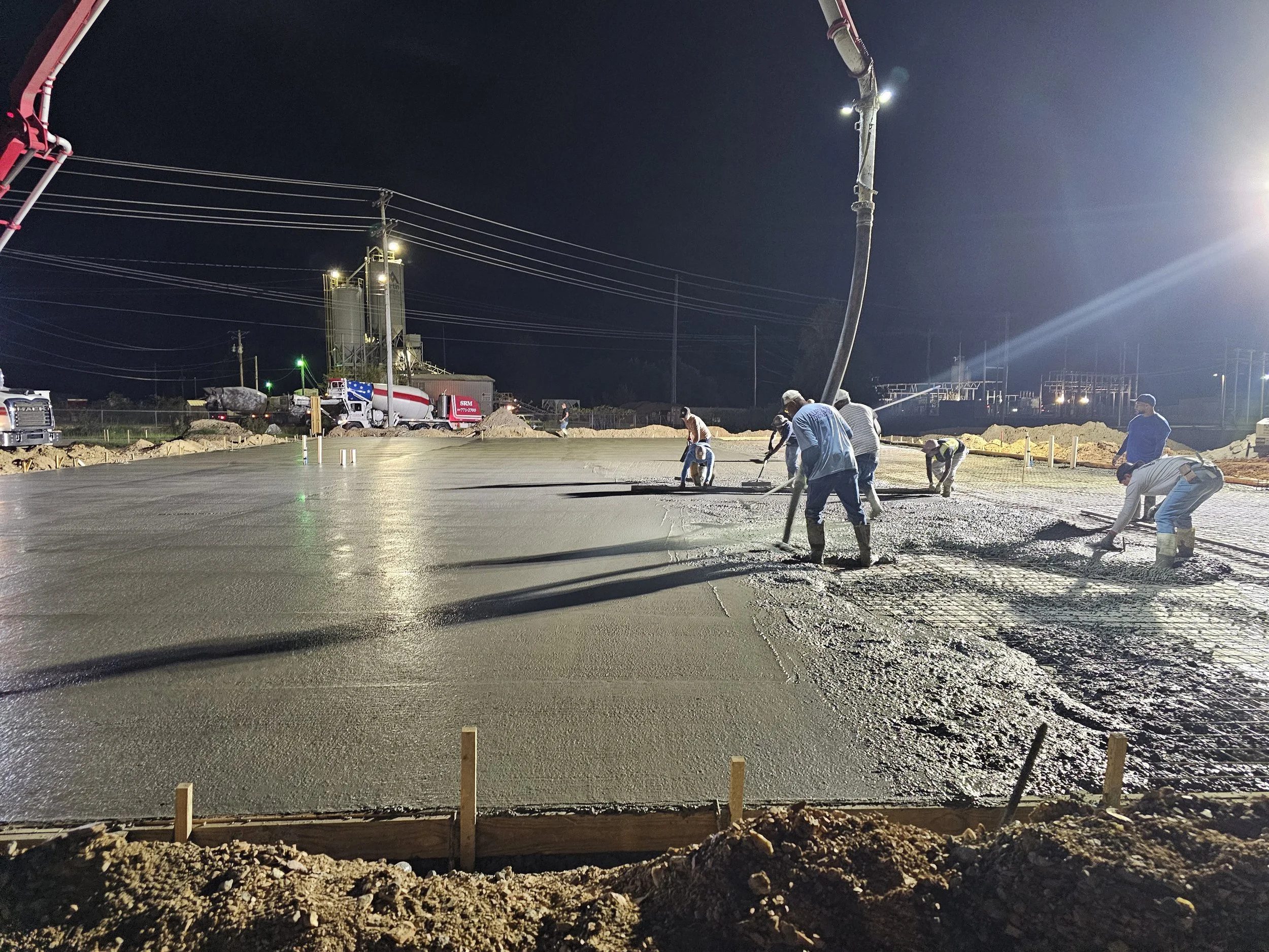 Workers pouring and leveling wet concrete at a construction site during night time.