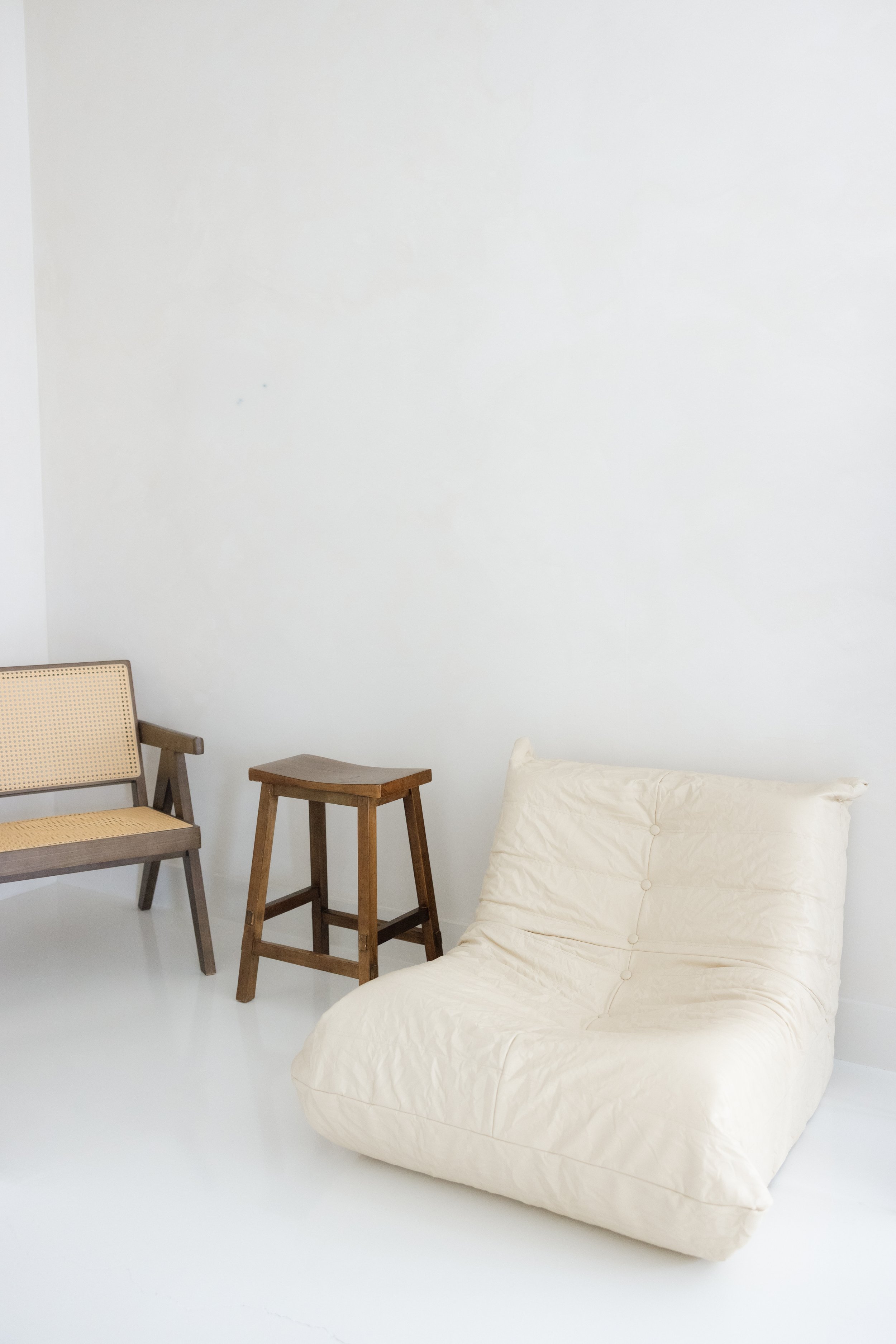 Minimalist white room with a cream bean bag chair, wooden stool, and chair.