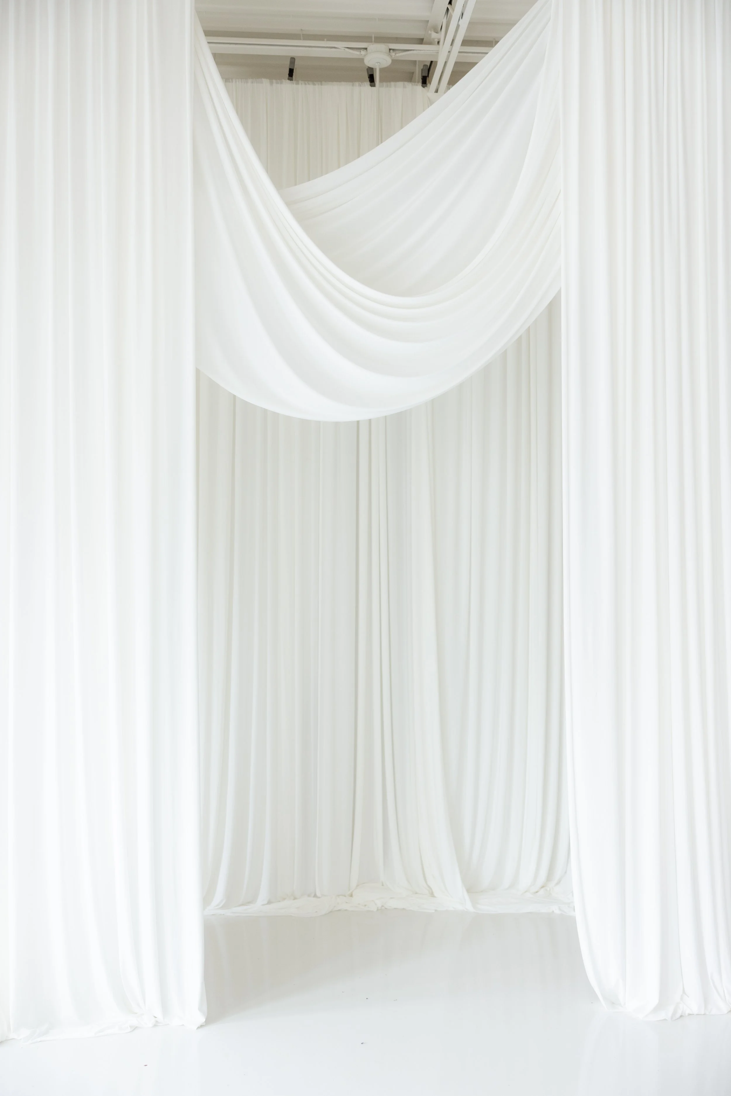 White draped fabric backdrop with flowing curtains in a bright, minimalist space.