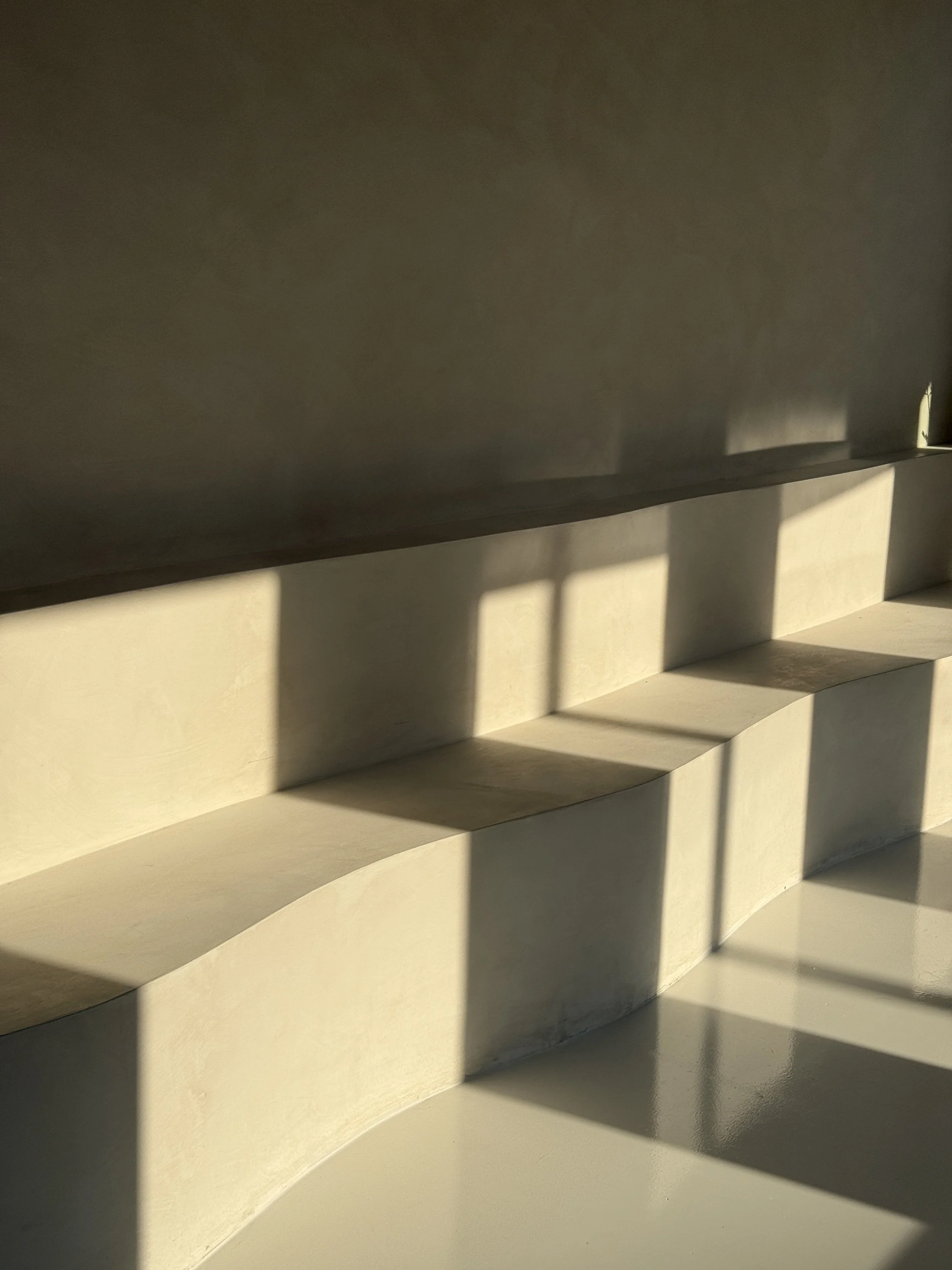 Sunlight casting shadows of window frames on a tiered beige wall or architectural structure.