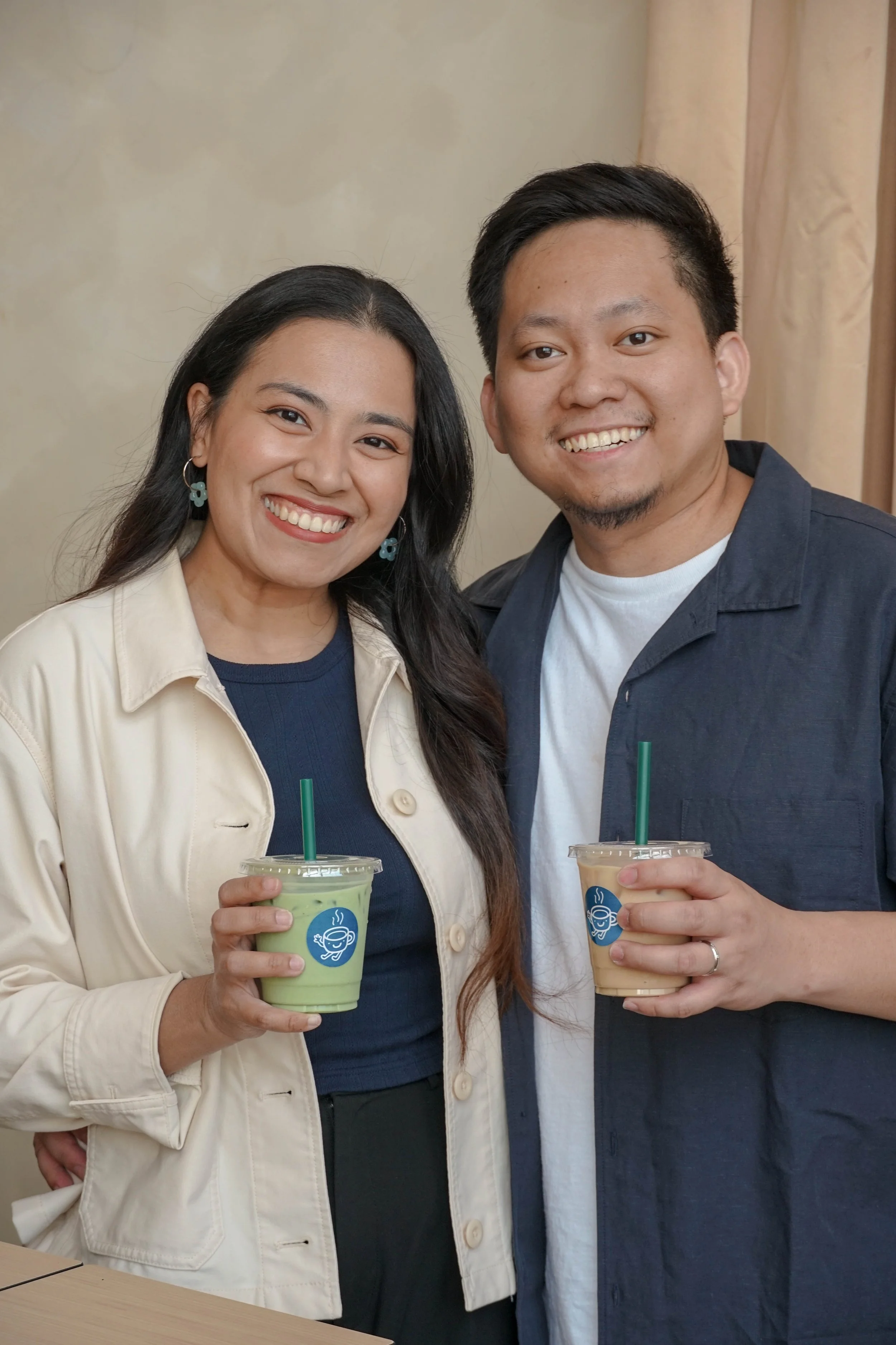Aries and Anna, owners of Newtown Avenue Coffee holding a matcha latte and a coffee latte
