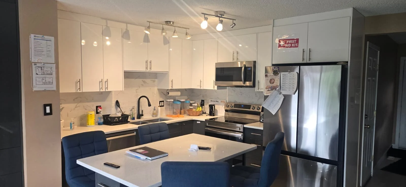 Modern kitchen with white cabinets, stainless steel refrigerator, black and gray accents, and a kitchen island with chairs.