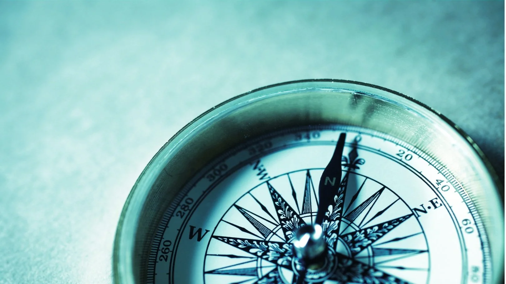 A close-up of a compass showing north at the top, set against a textured, light-colored background.
