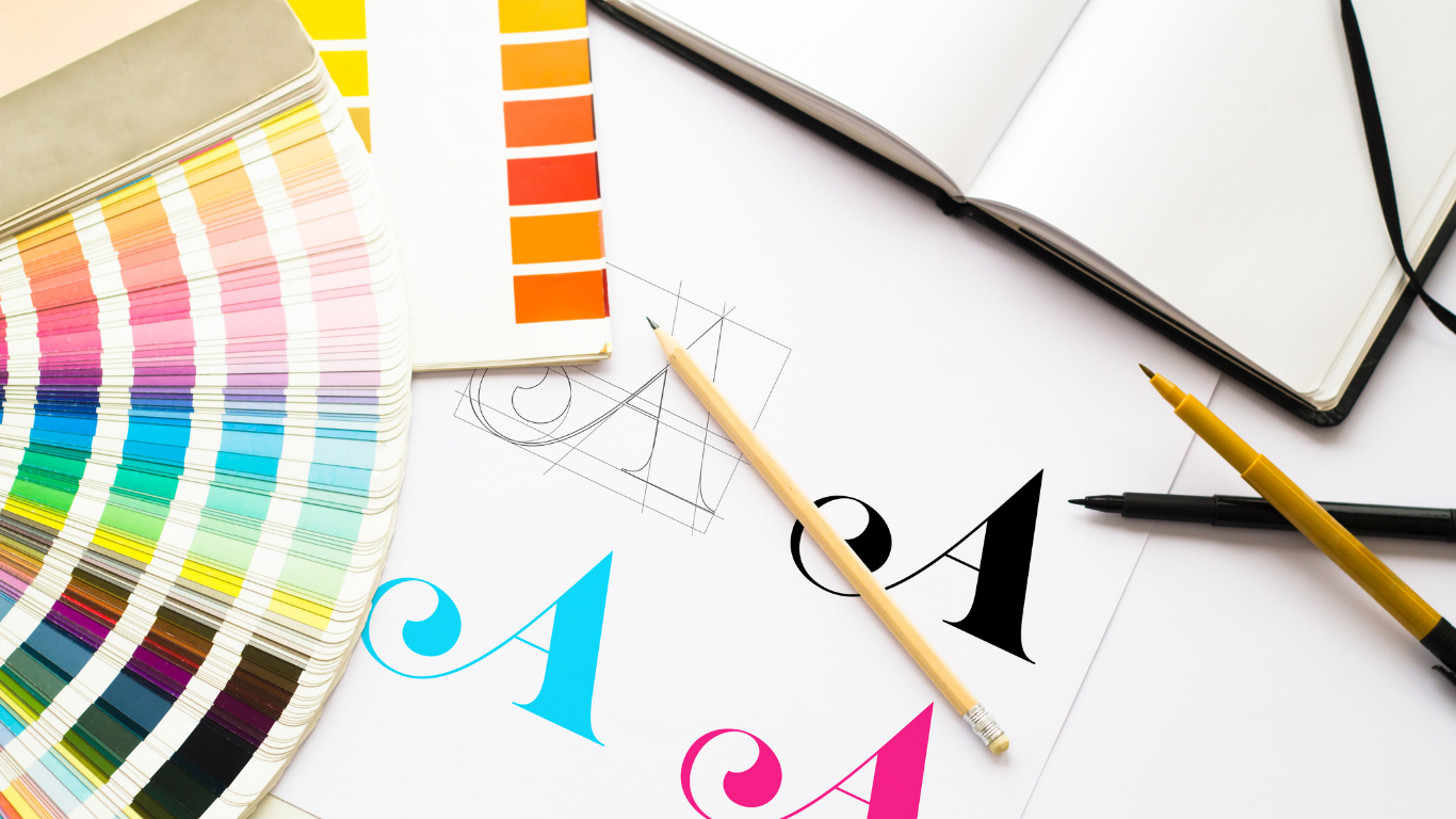 Color swatch book, design sketches, and pens on a white surface.