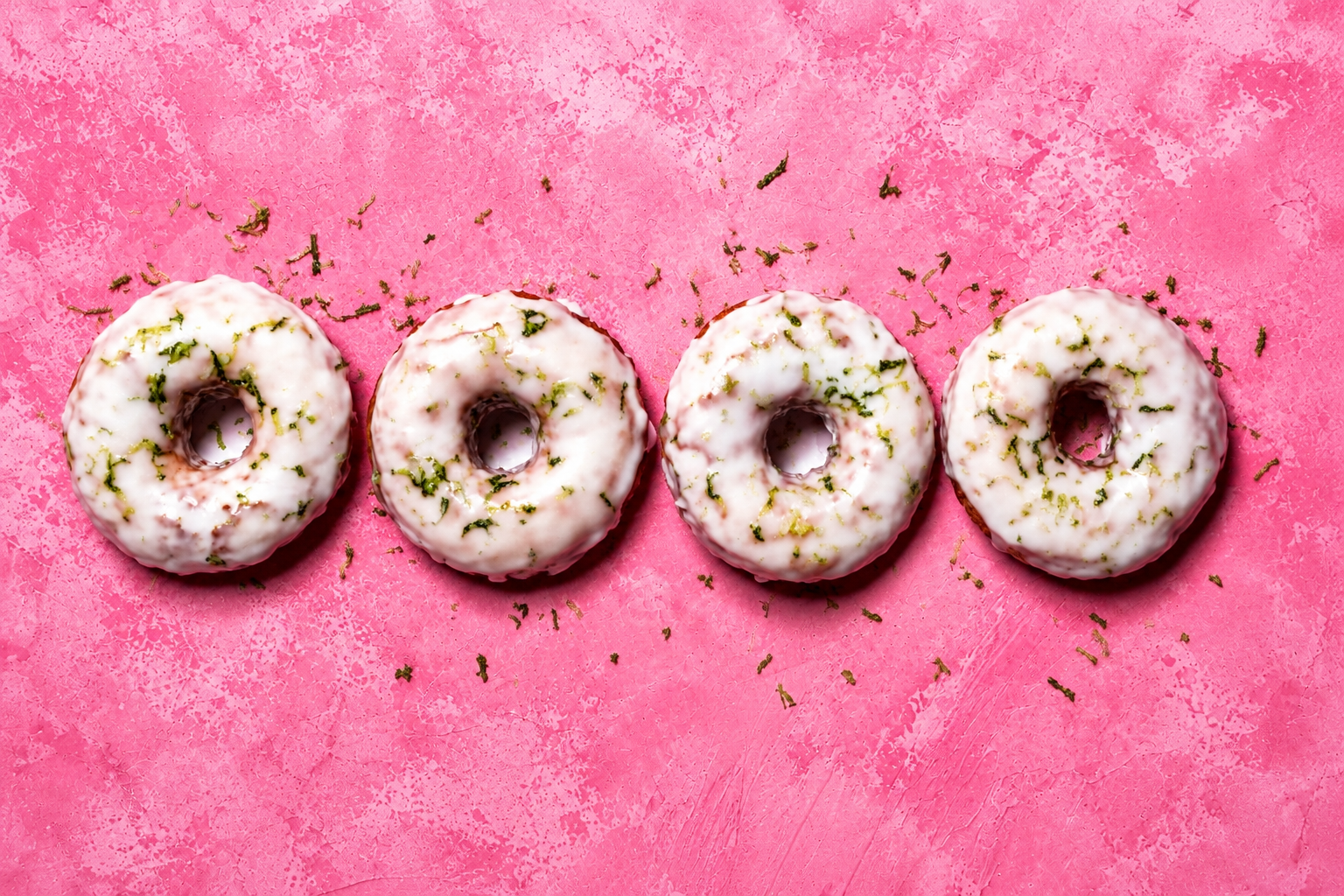 Four white-glazed donuts on pink