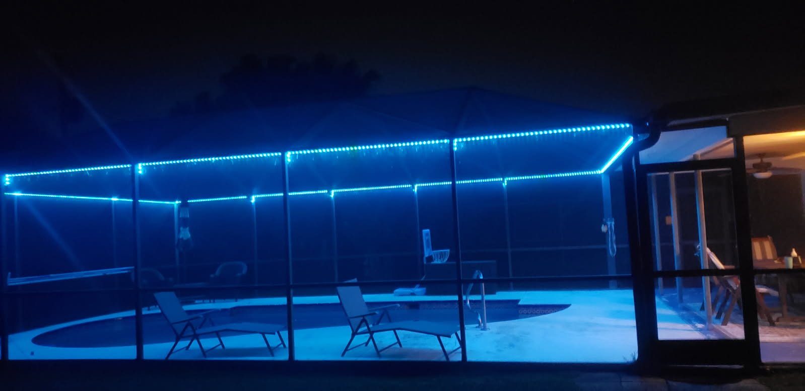 Outdoor pool area with blue LED lights at night, installed on an enclosed screened structure.
