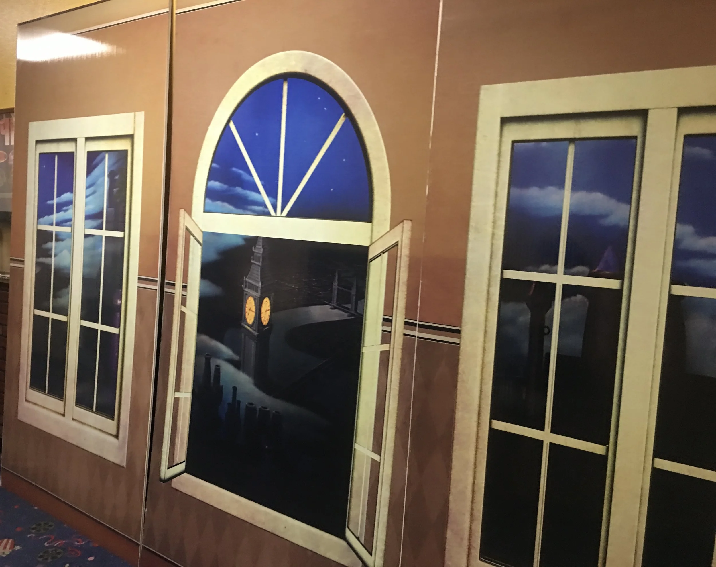 A mural or painting of the Eiffel Tower seen through large framed windows with clouds in the sky.