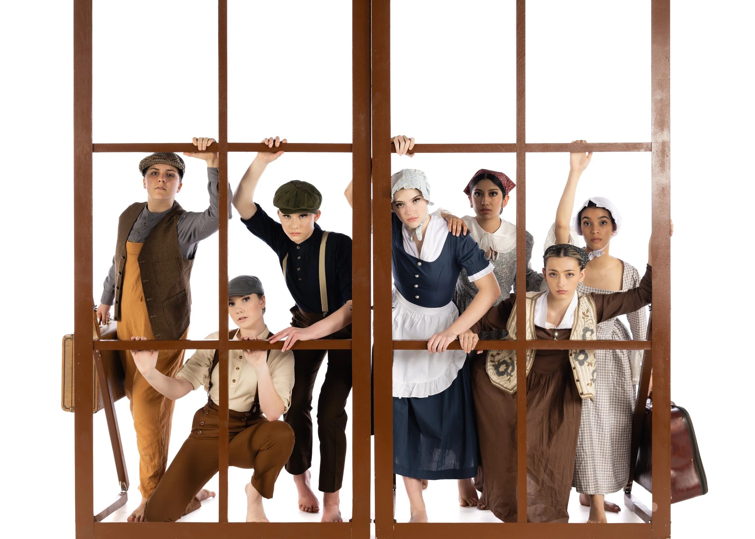 Group of children dressed in historical costumes standing behind a large wooden jail cell.
