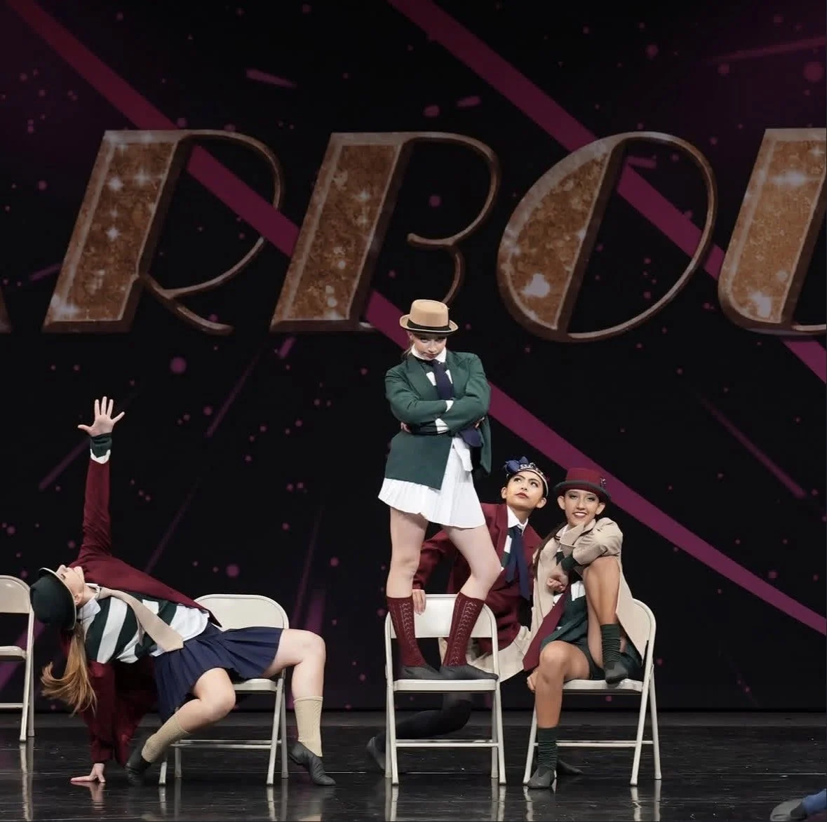 Dance troupe performing on stage with a large comic-style backdrop in the background.