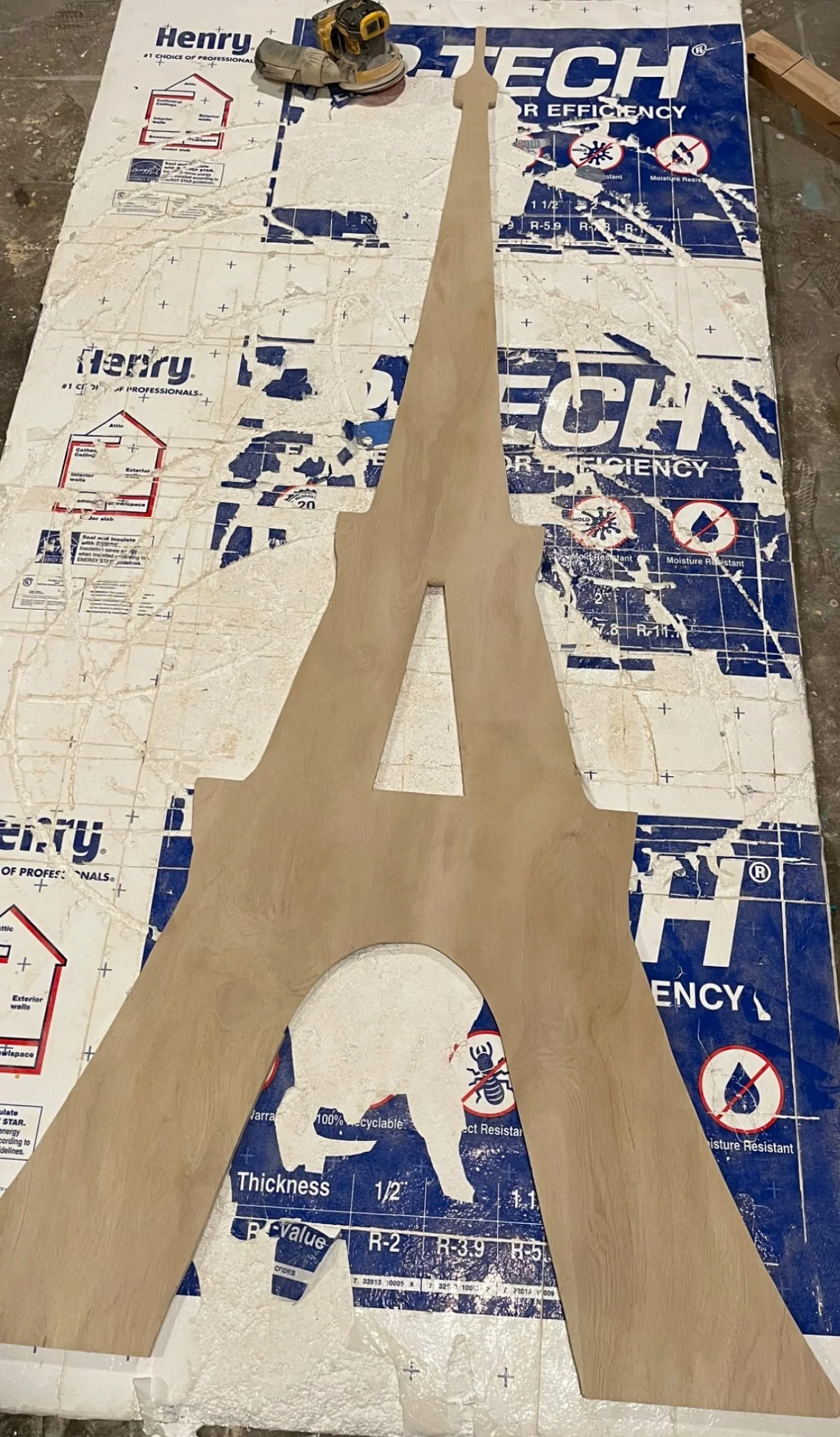 Wooden cutout of the Eiffel Tower placed on a torn and dirty blue and white branded insulation sheet.