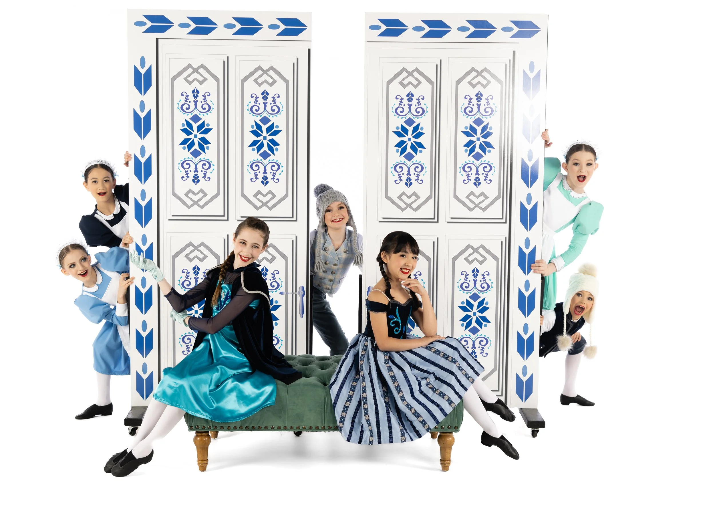 Group of young girls dressed in princess costumes, posing around a decorative prop resembling a palace or castle with blue and white designs.