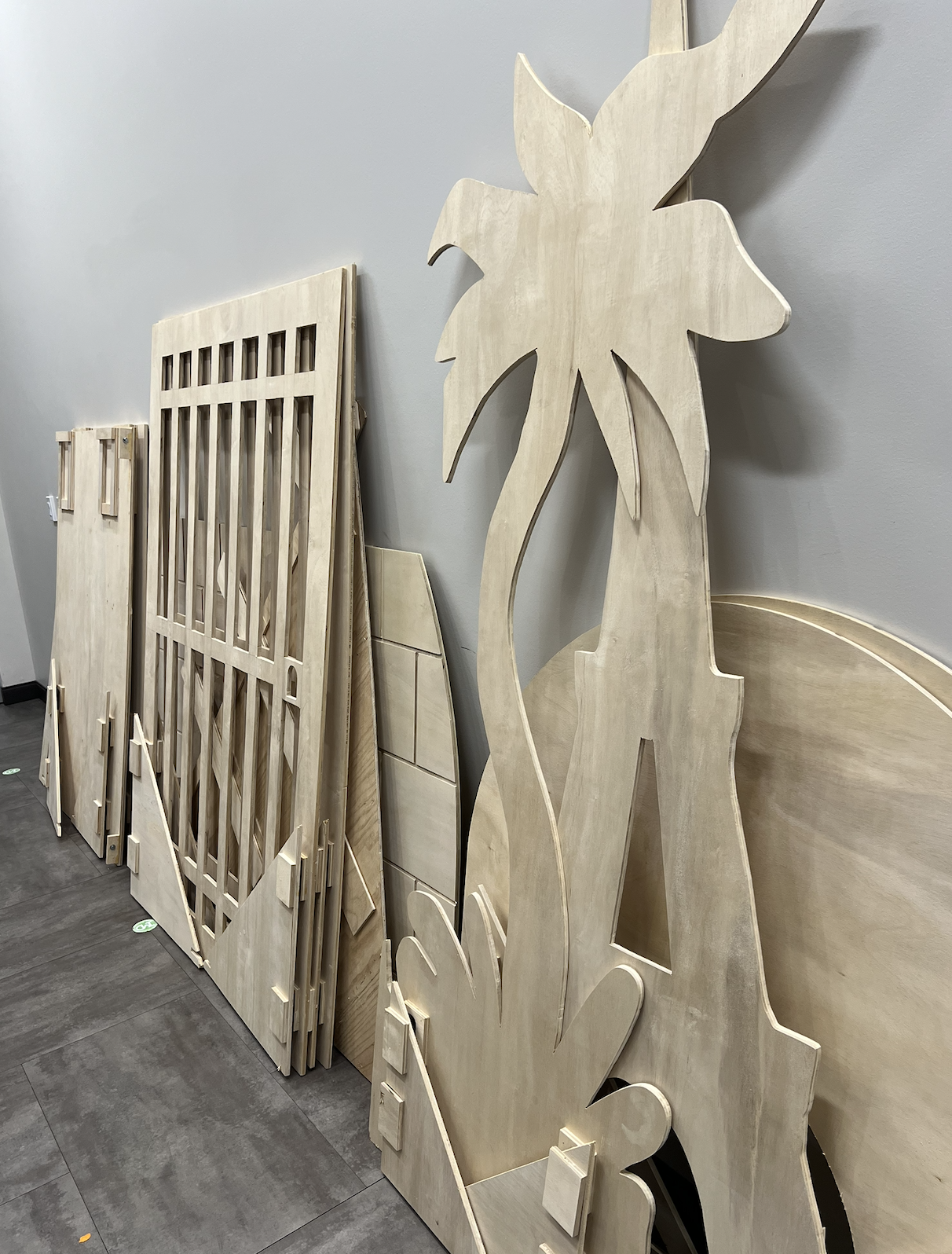Unfinished wooden furniture parts, including a large palm tree cutout, leaning against a wall in a store or workshop.