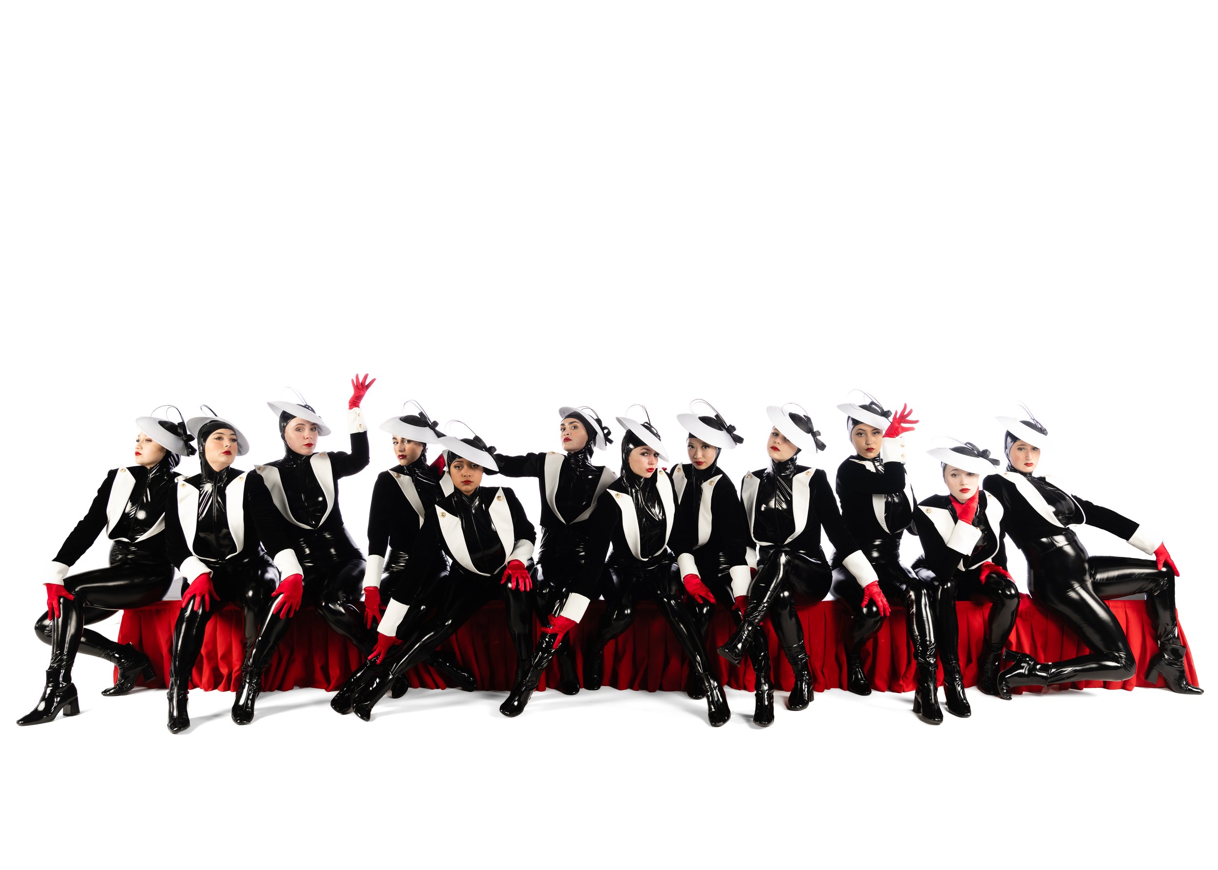 Group of women in black, white, red, and shiny costumes with hats, gloves, and high boots, posing together against a white background.