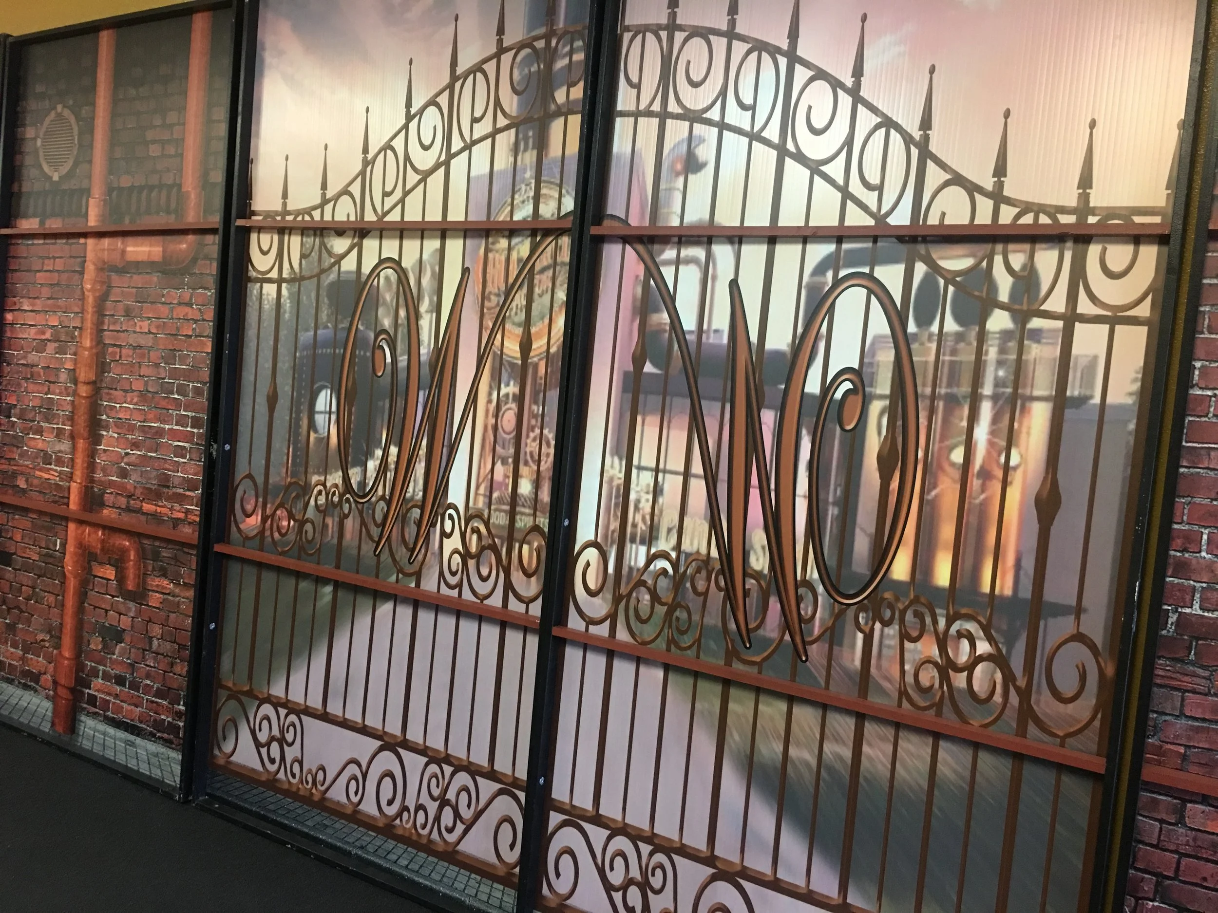 Display of decorative iron gates mounted on a brick wall with a background of a storefront window reflection.