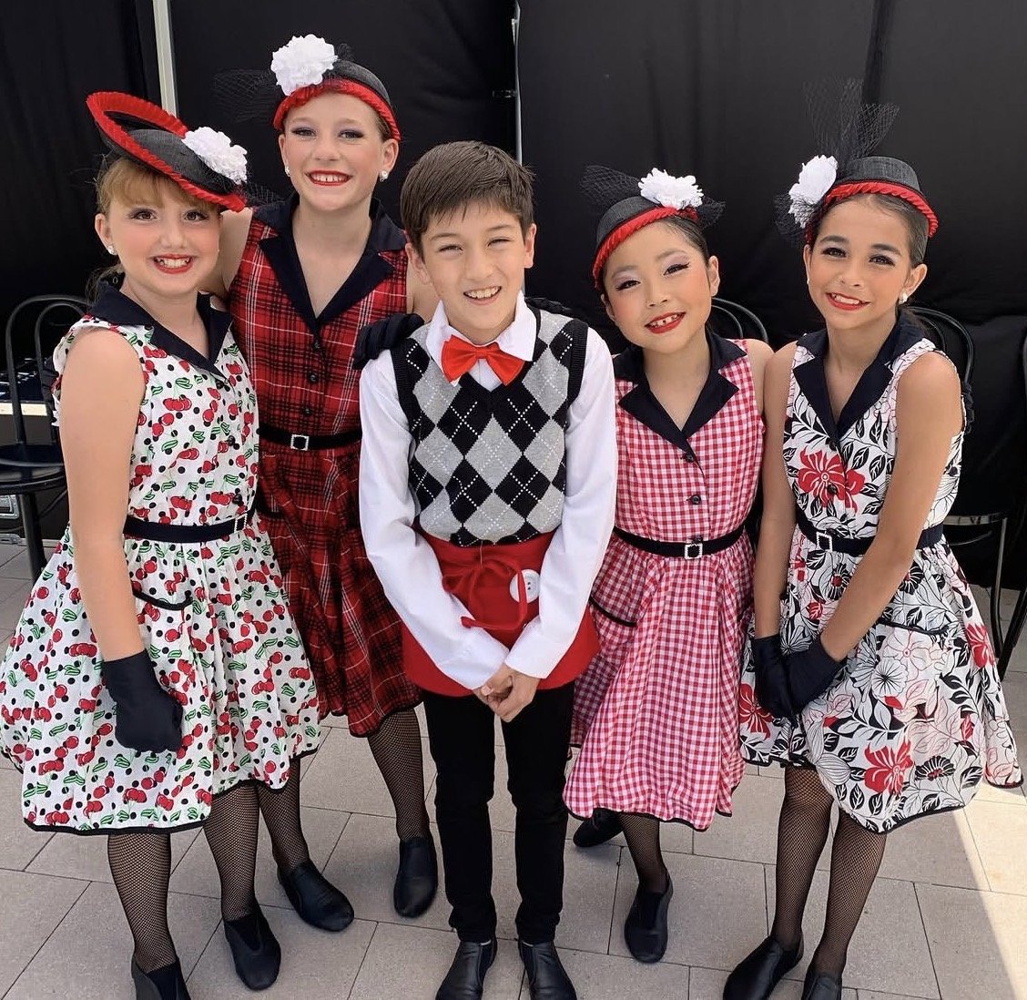 Group of five kids dressed in vintage style clothing, smiling and posing for a photo.