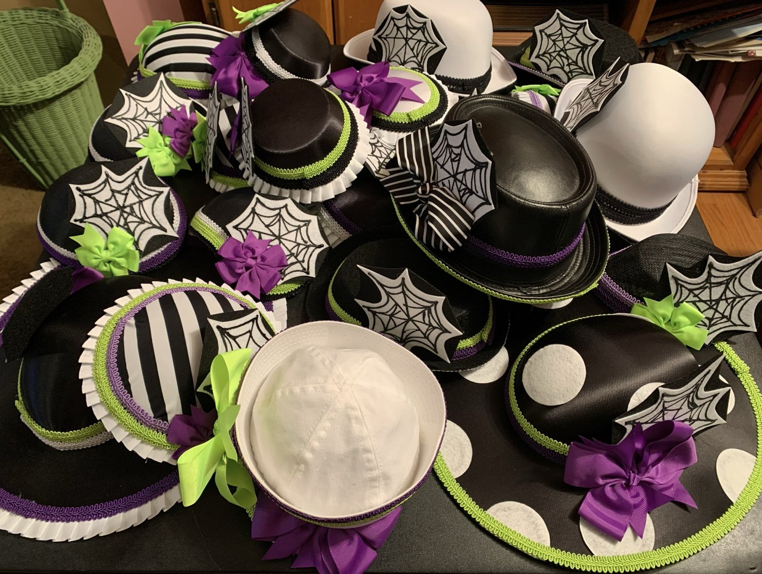 Collection of decorative hats and headbands with Halloween themed designs, including spiderwebs, bows, and polka dots in black, white, purple, and green.