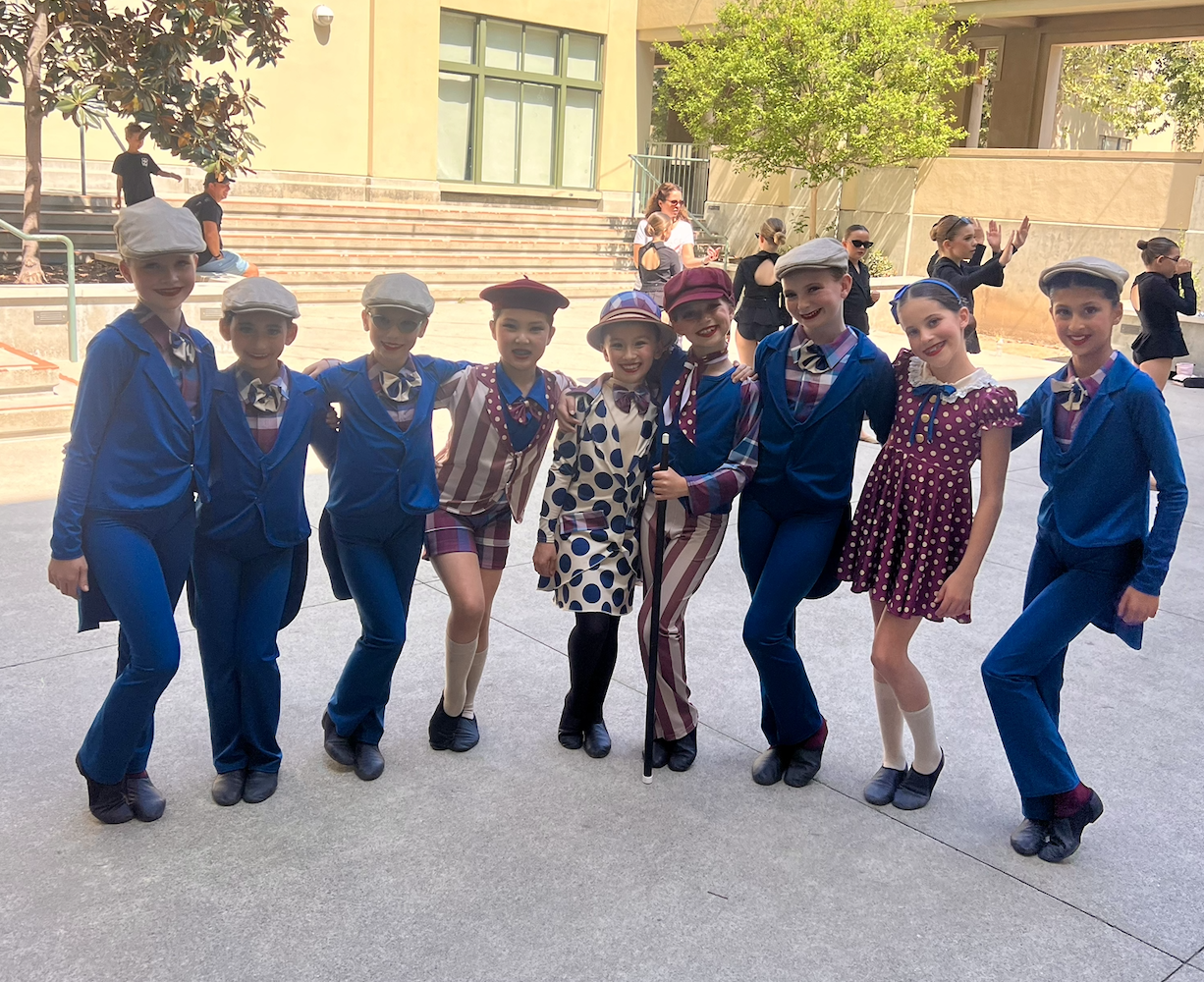 Children dressed in vintage-style costumes, smiling and posing together outdoors.