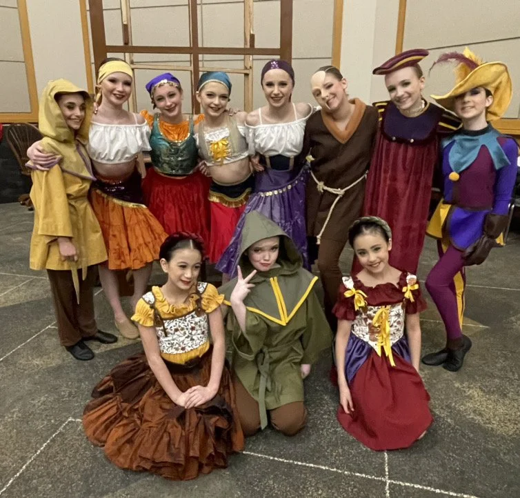 Group of children in colorful costumes, some dressed as knights, princesses and fantasy characters, posing together indoors.
