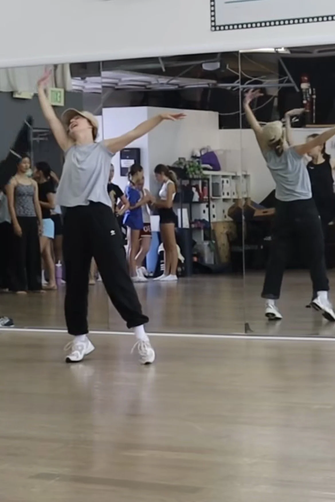 People dancing in a dance studio with mirrors on the wall and wooden floors, some observers in the background.