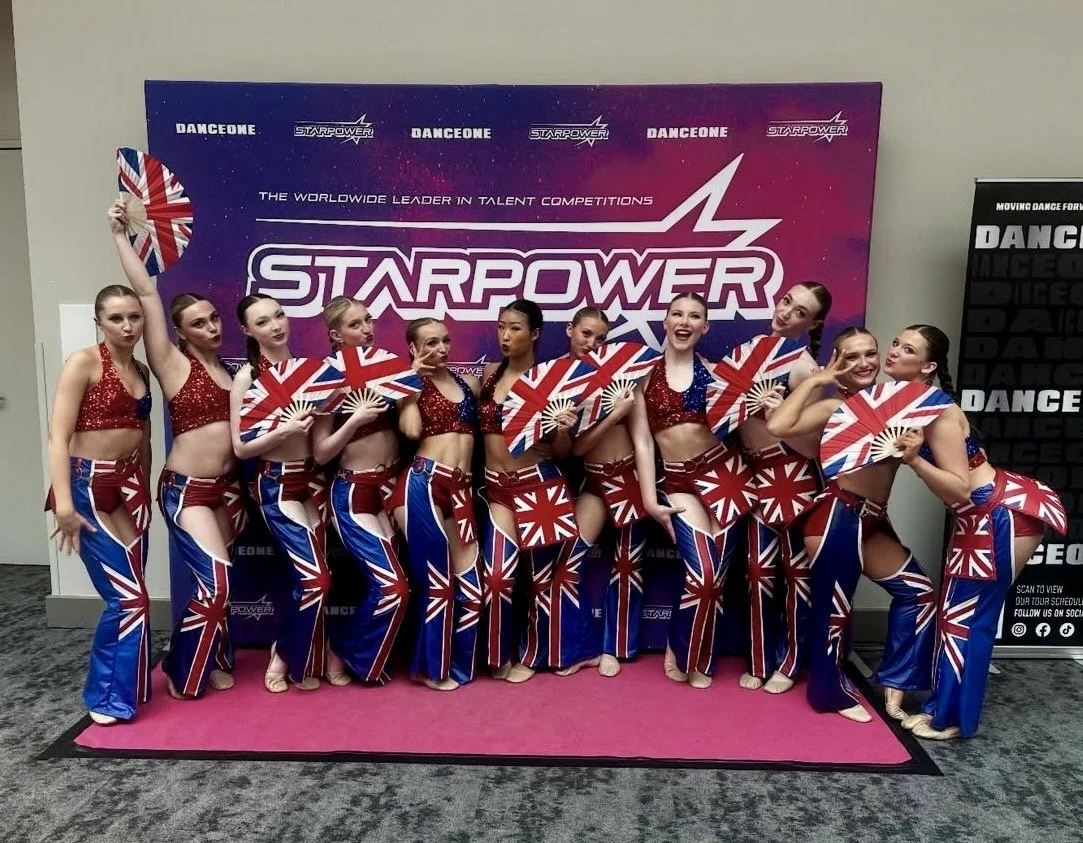 A group of cheerleaders in red, white, and blue costumes with Union Jack flags, posing in front of a Starpower competition backdrop.