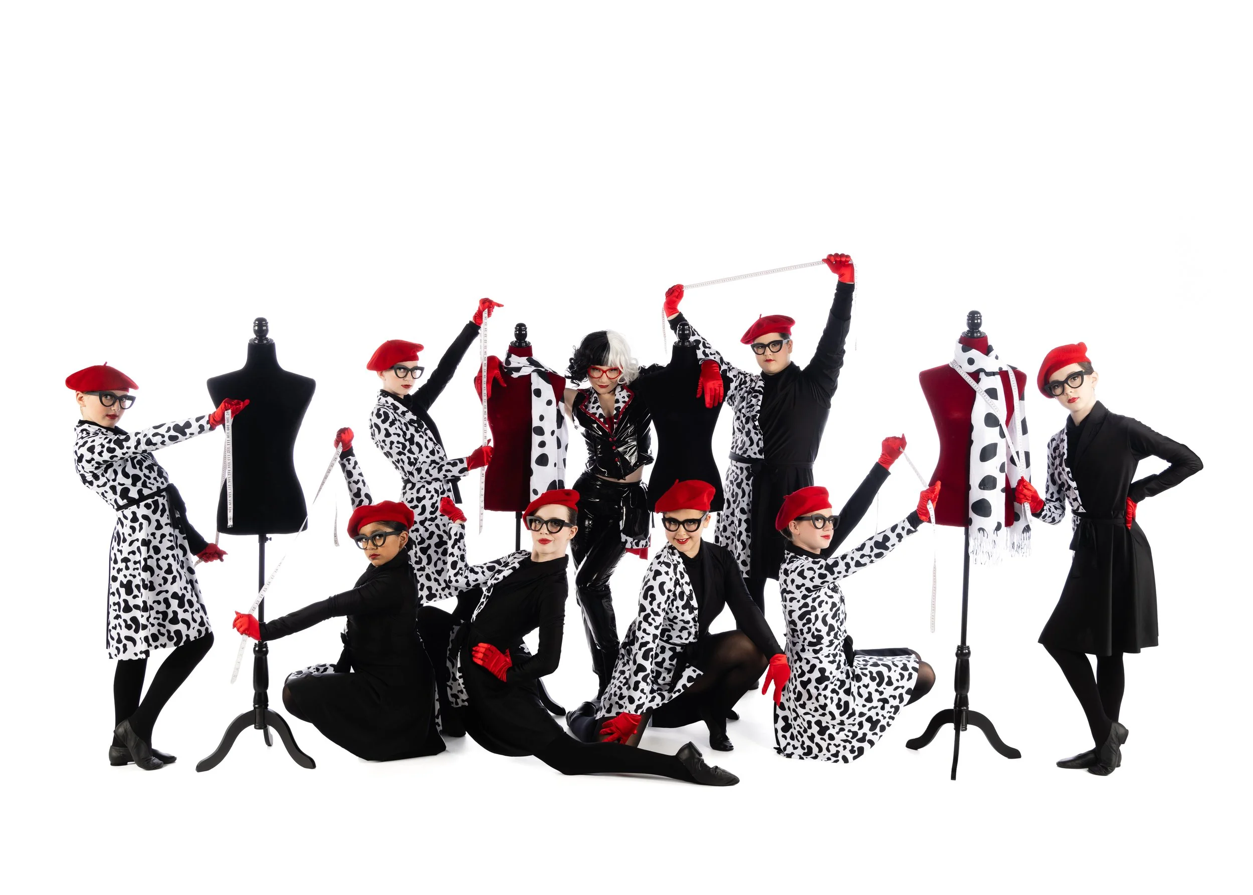 Group of fashion models dressed in Dalmatian print outfits with red berets, glasses, and gloves, posing around mannequins against a white background.