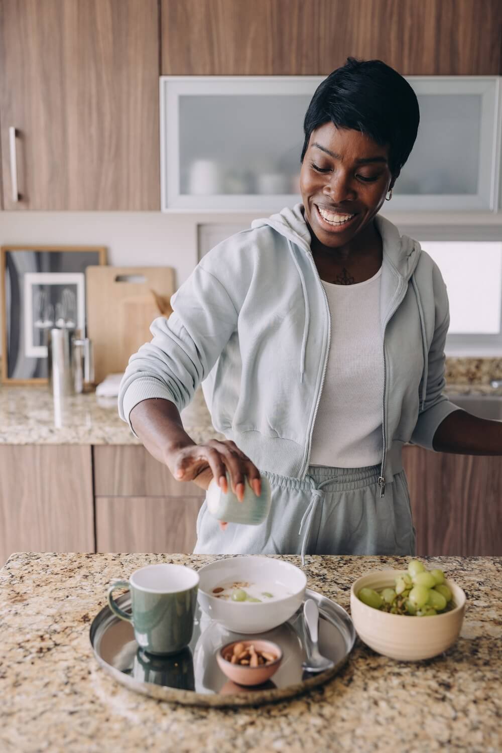 A woman stirring her breakfast in the kitchen, with a bowl of grapes and other breakfast items on the counter.