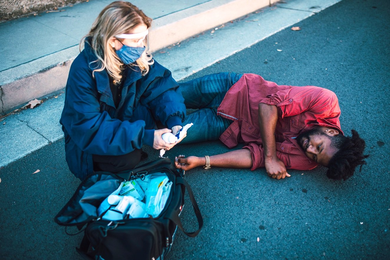 A woman prepares to conduct first aid on a man lying on the pavement.
