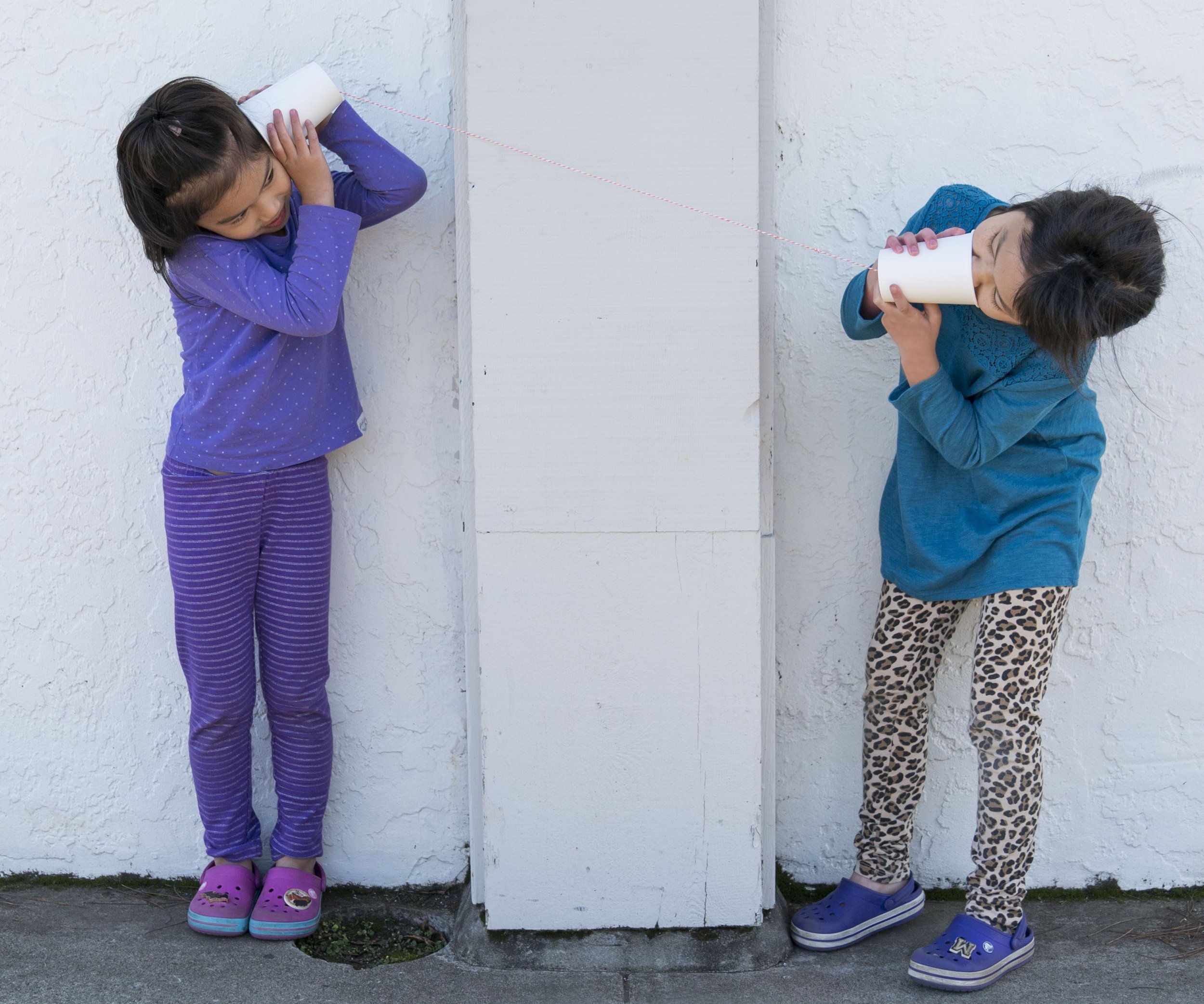 Two little girls communicate through a string phone.