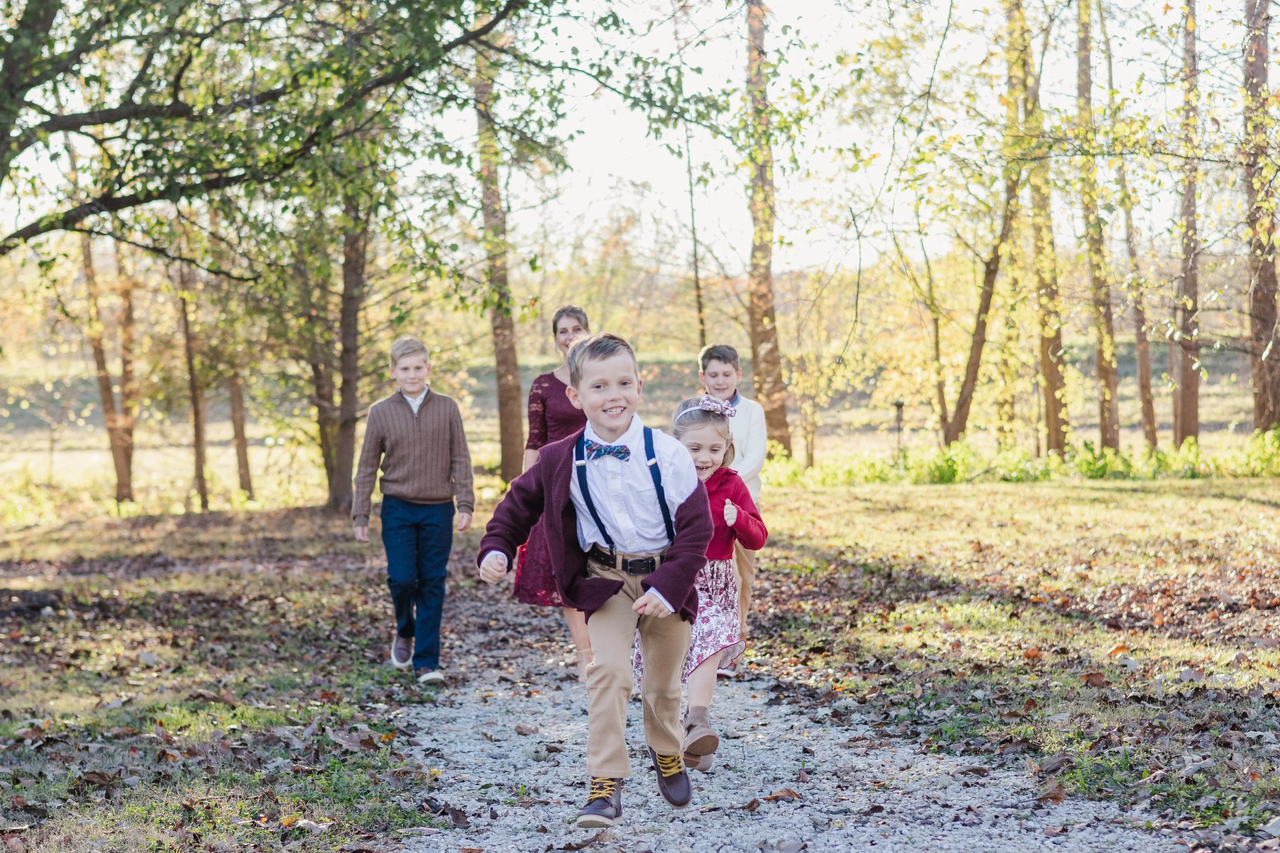 Children running on a dirt path through a wooded area on a sunny day.