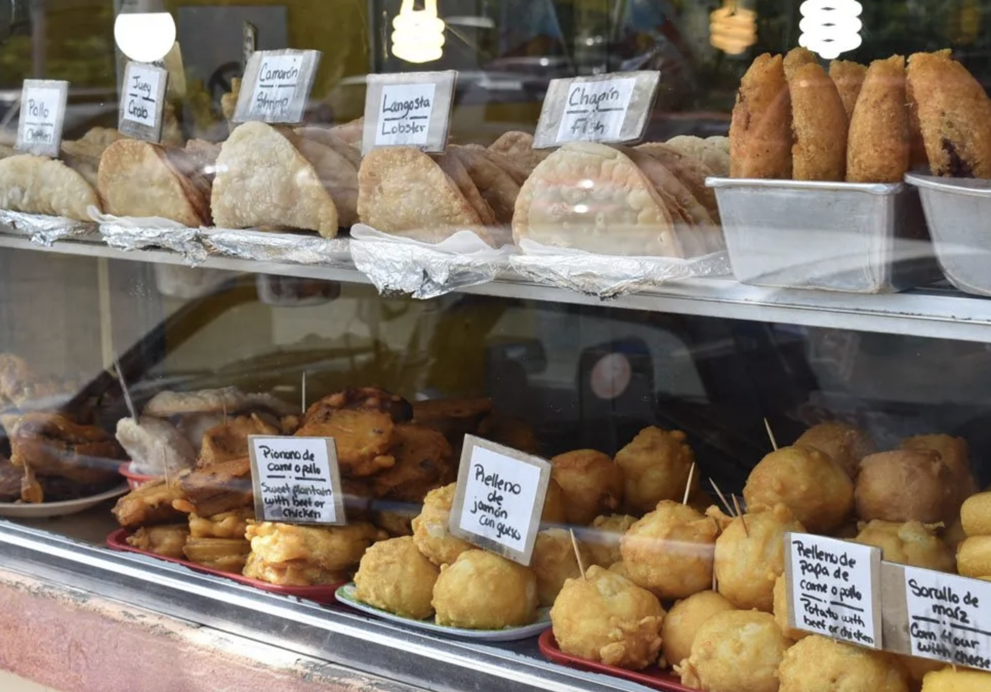Display case with traditional Mexican foods including empanadas, stuffed pastries, and fried items labeled in Spanish such as 'Piquito de pollo' and 'Relleno de jamón con queso'.