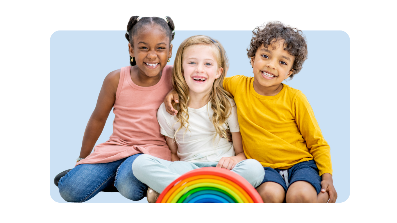 Three children sitting together, smiling, with a rainbow-shaped toy in front of them, against a light blue background.