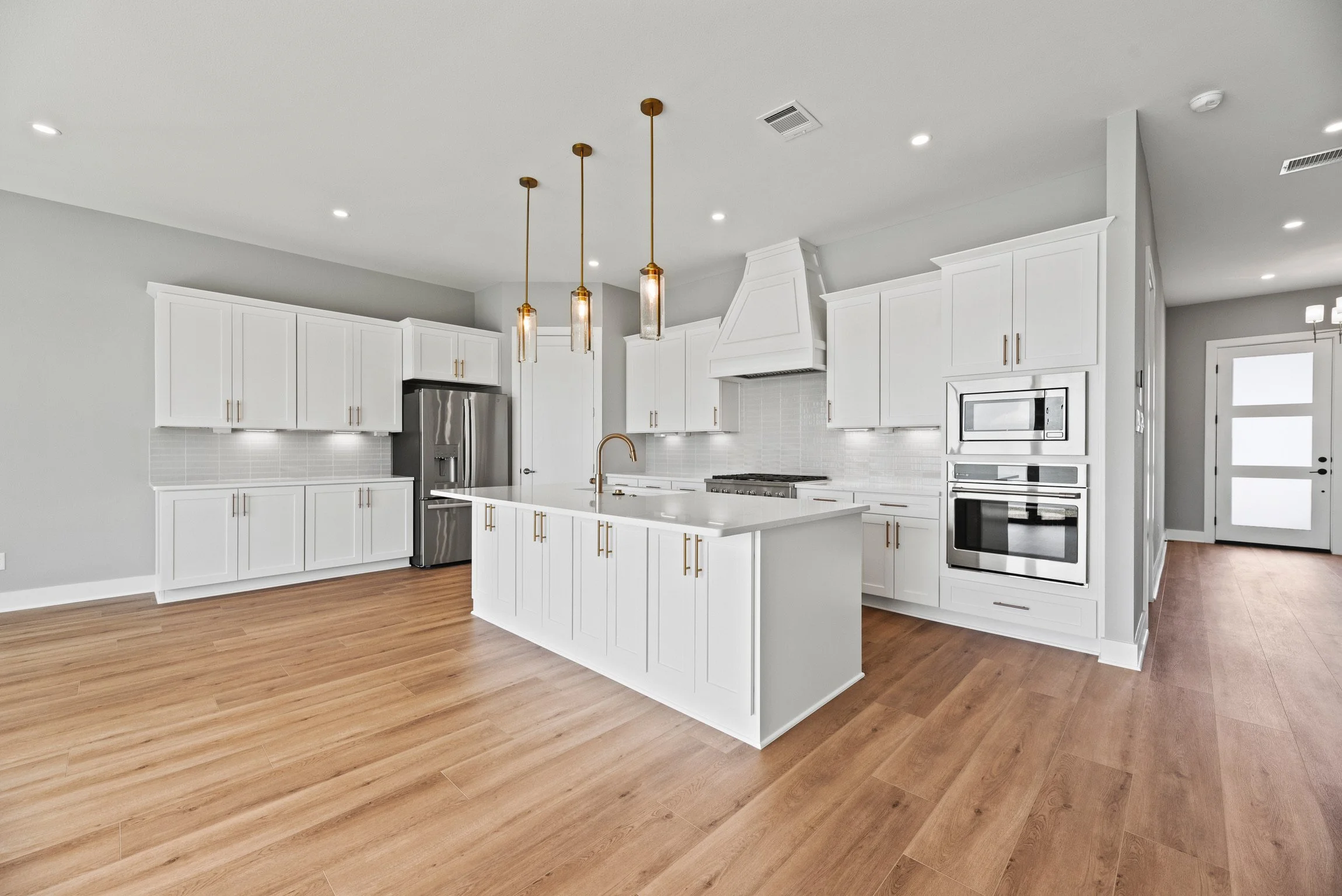 Modern kitchen with white cabinets, stainless steel appliances, wooden flooring, and pendant lighting.
