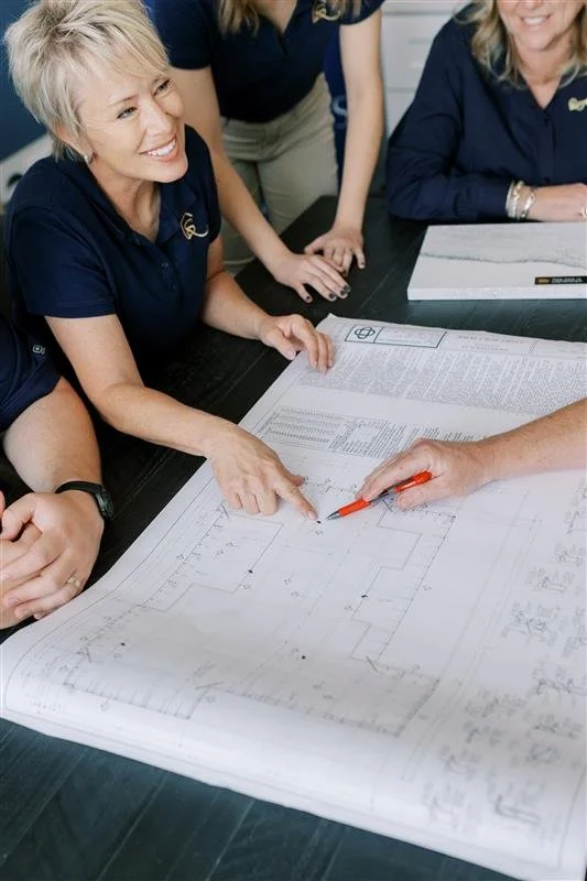 Group of women reviewing blueprints on a table during a meeting.