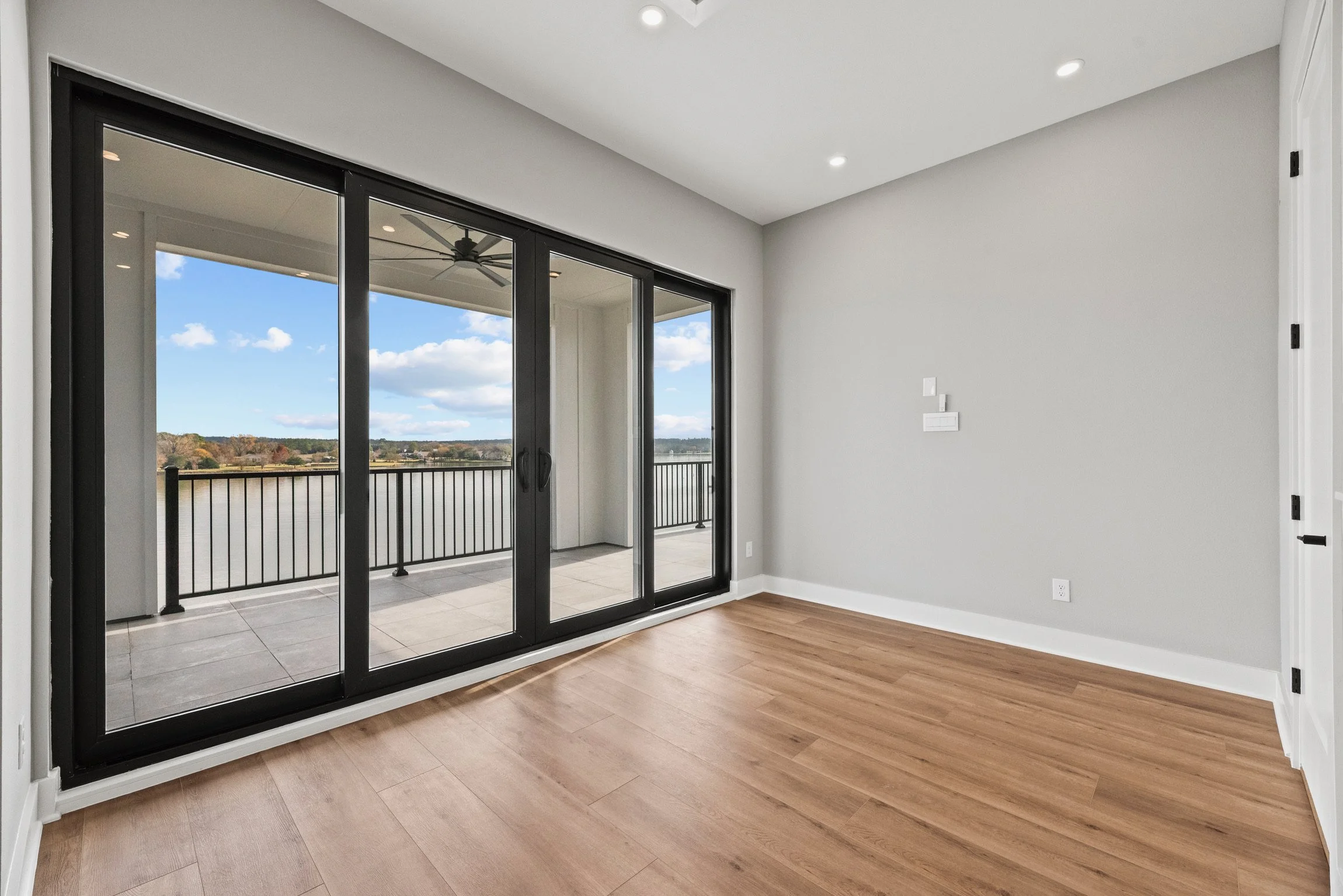 Empty room with light gray walls, wood flooring, and large sliding glass doors leading to a balcony with a water and landscape view.